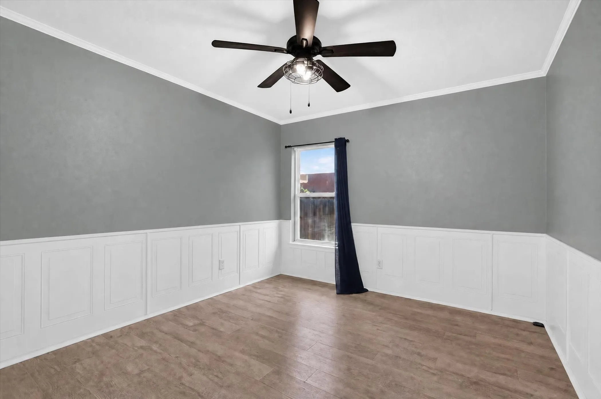 Wood-finish flooring, wainscoting, crown molding, and a ceiling fan with integrated lighting
