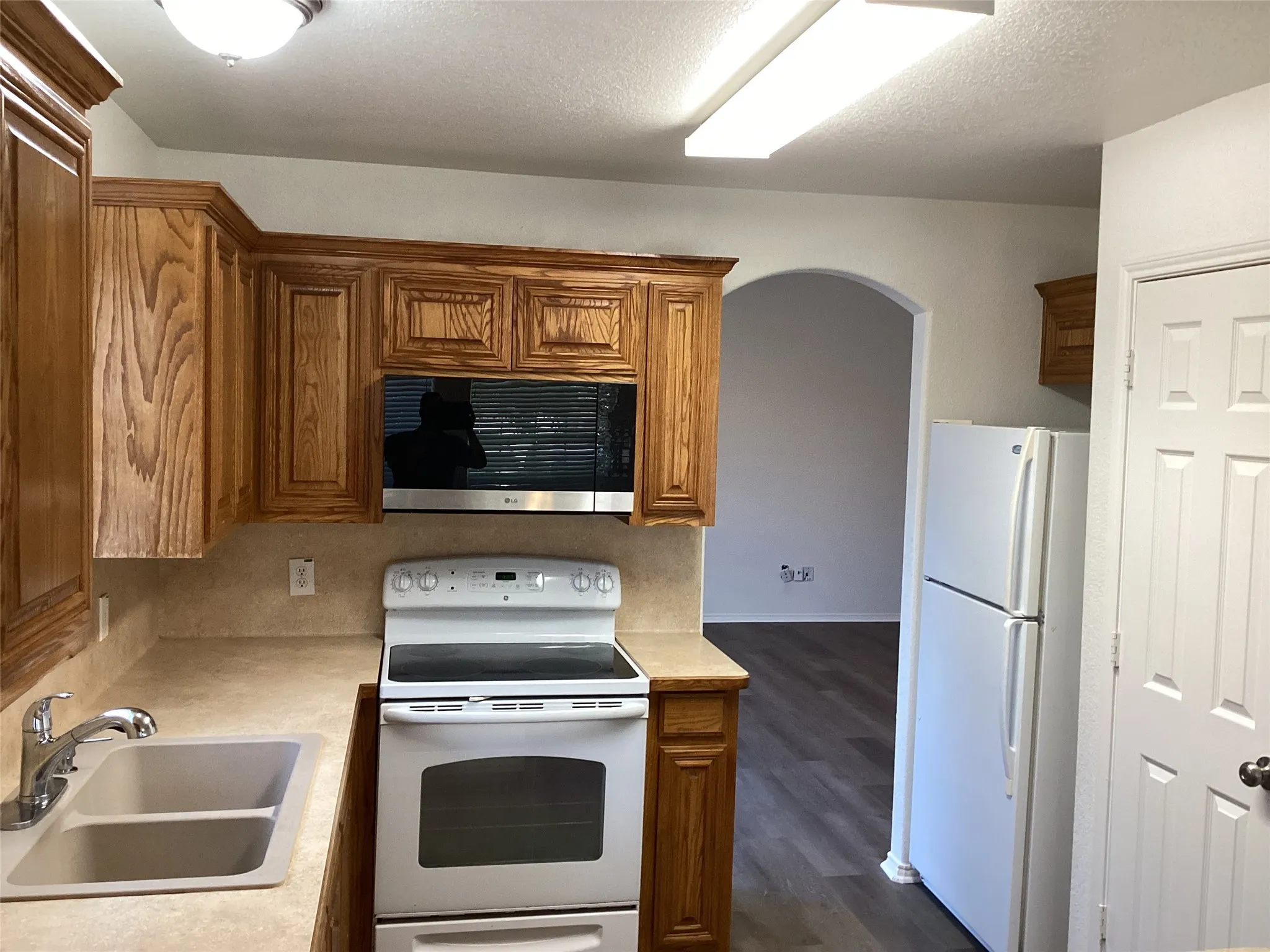 Kitchen featuring wood cabinetry, a stainless steel microwave, a white electric range, a double basin sink with a chrome faucet, and wood-finish flooring