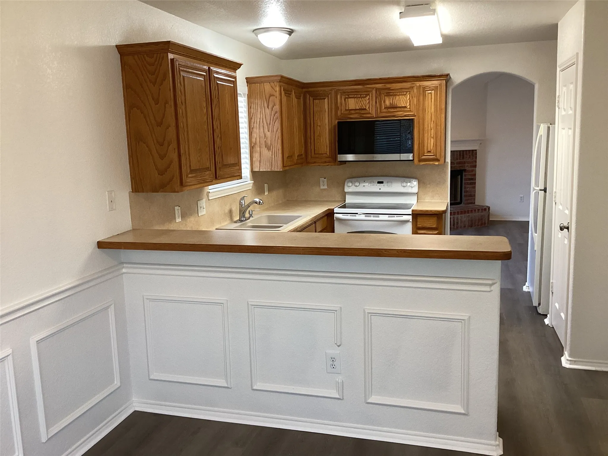 U-shaped kitchen with wood-finish cabinetry, built-in microwave, white electric range, and wood-finish flooring