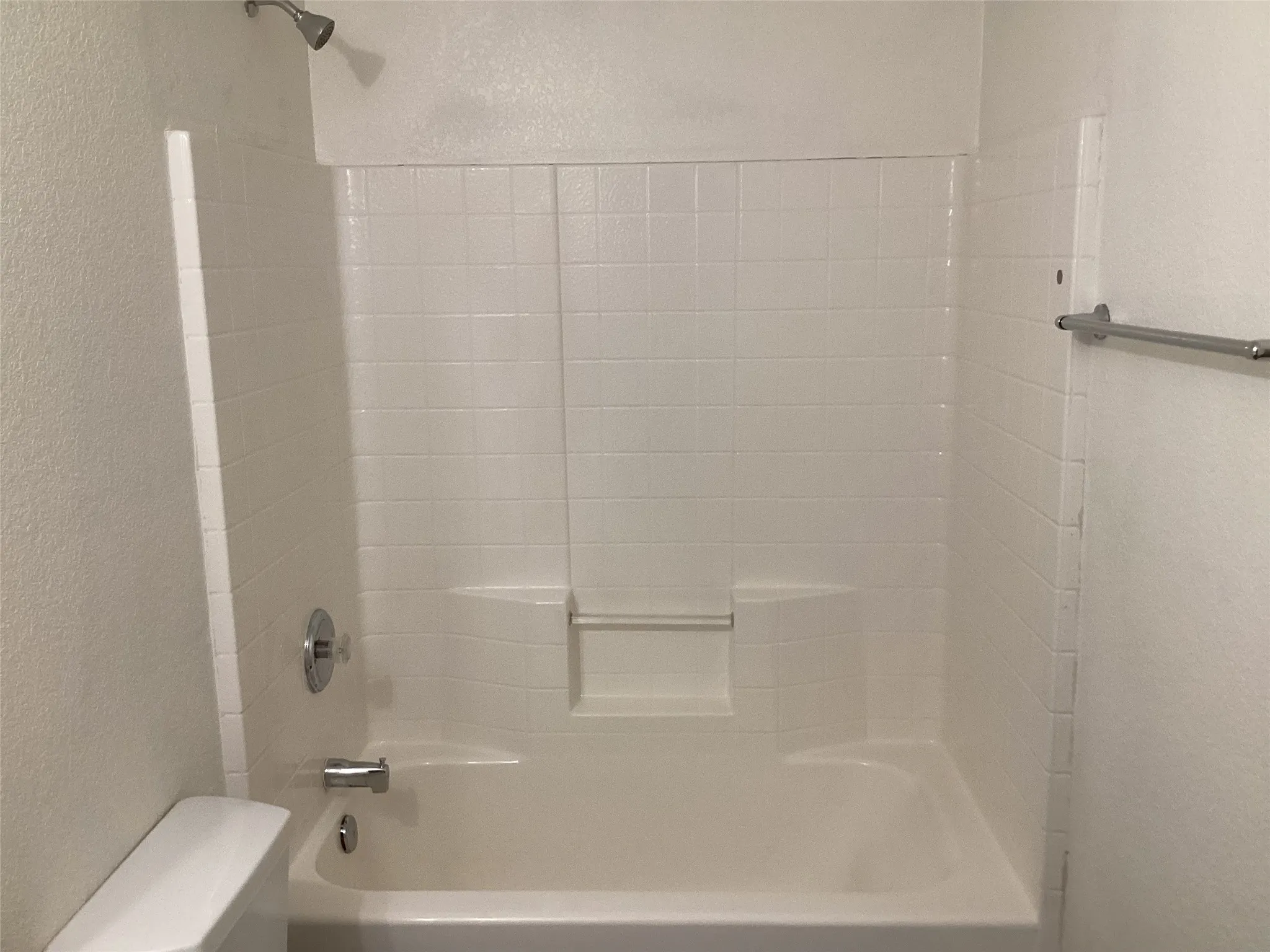 White tile shower surround with integrated soap dish, chrome showerhead, and a coordinating chrome towel bar