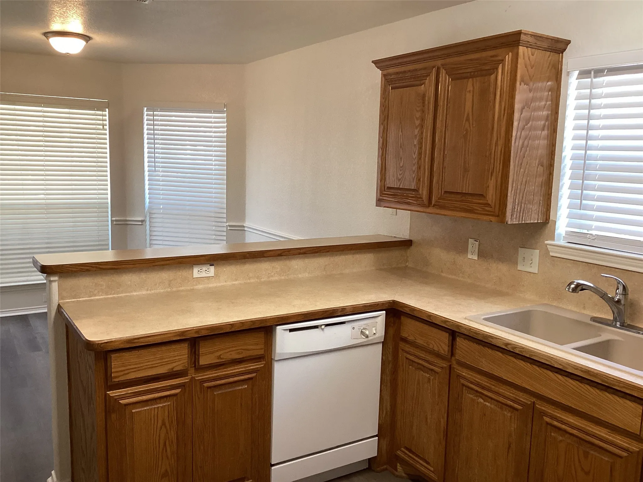 Kitchen featuring wood-finish cabinetry, a double basin sink, and a white dishwasher