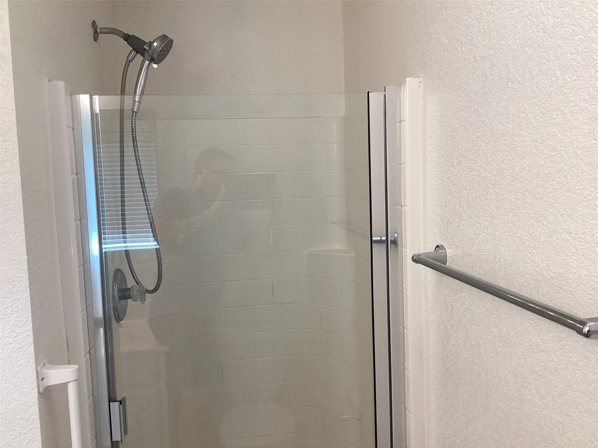 Shower enclosure with clear glass doors, subway tile-patterned shower surround, and a chrome-finish shower head with a handheld sprayer