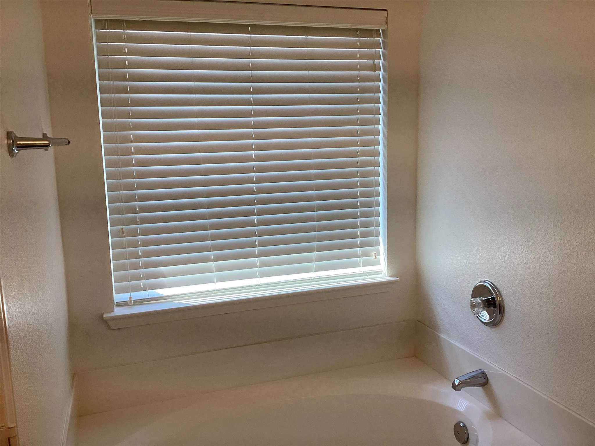 Bathtub with polished chrome fixtures, integrated window, and horizontal blinds
