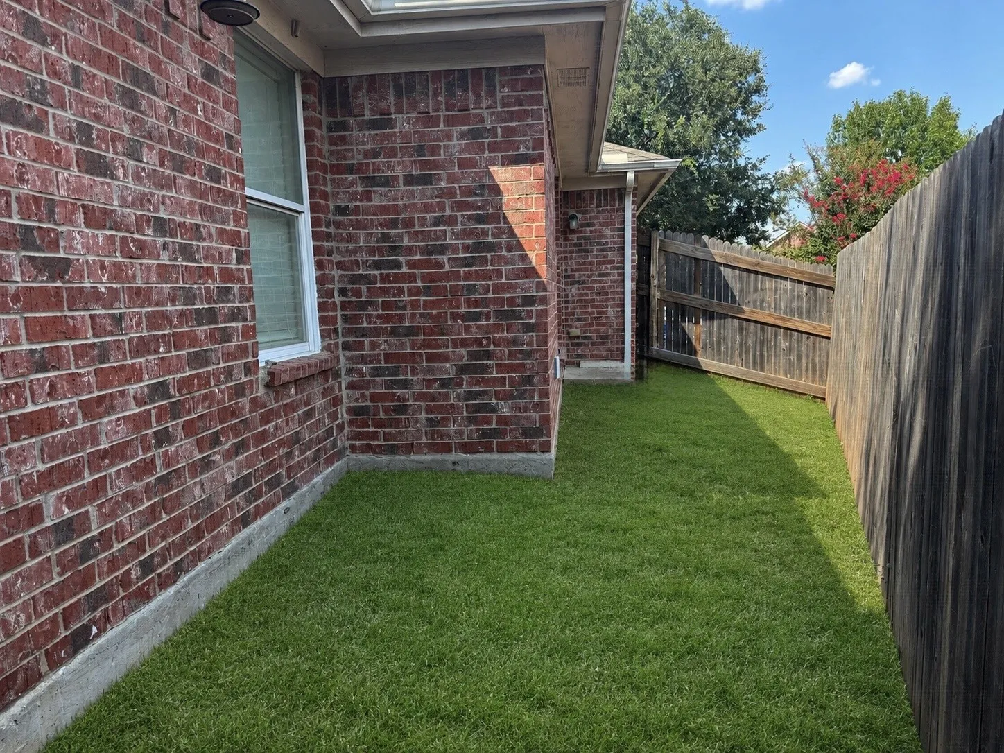 Brick exterior wall, white window frame, manicured lawn, wood fencing, gutter system
