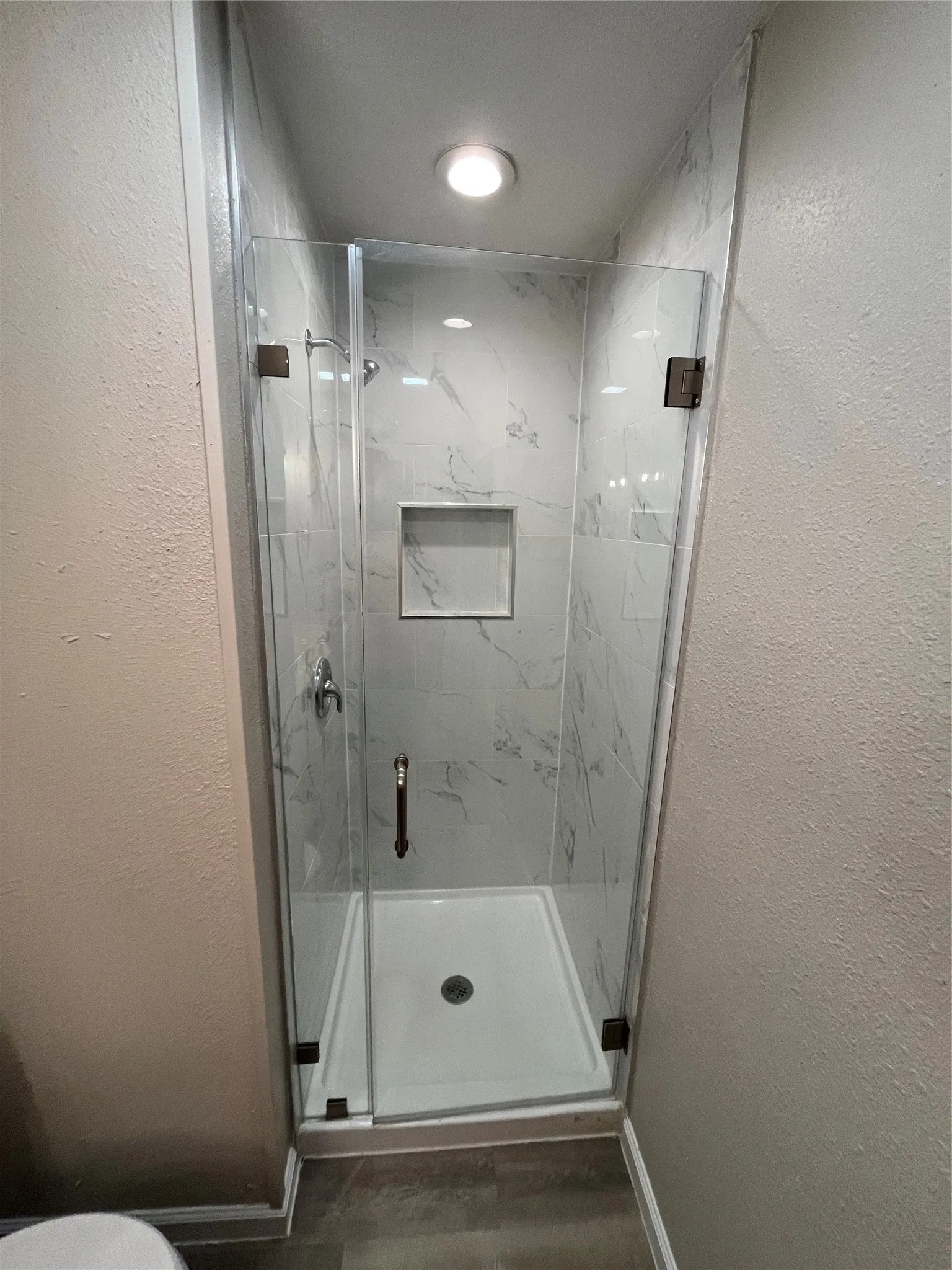 Glass-enclosed shower with white tiled walls, a built-in shower niche, and a white shower pan