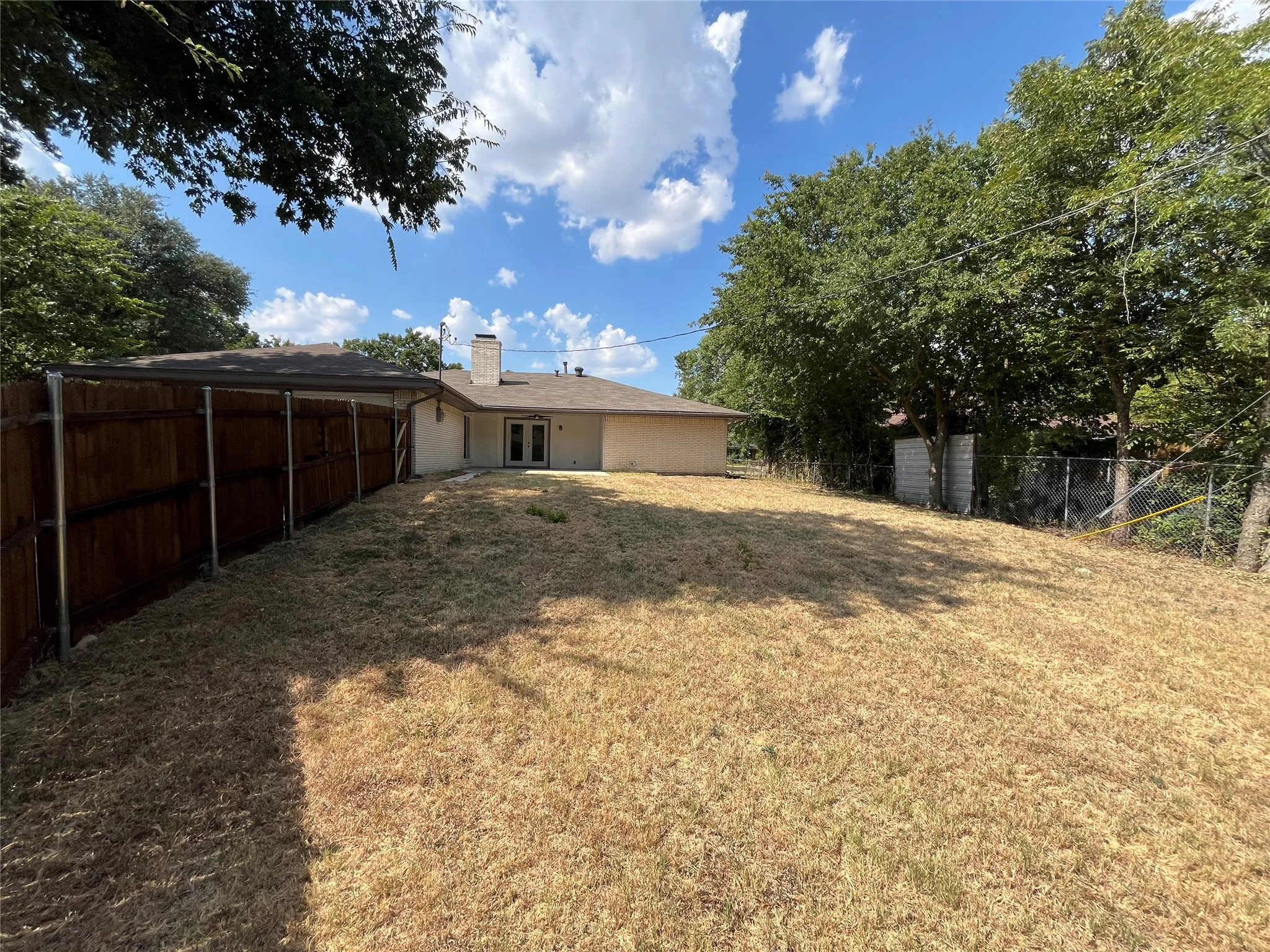 Expansive backyard with a covered patio structure and mature perimeter trees