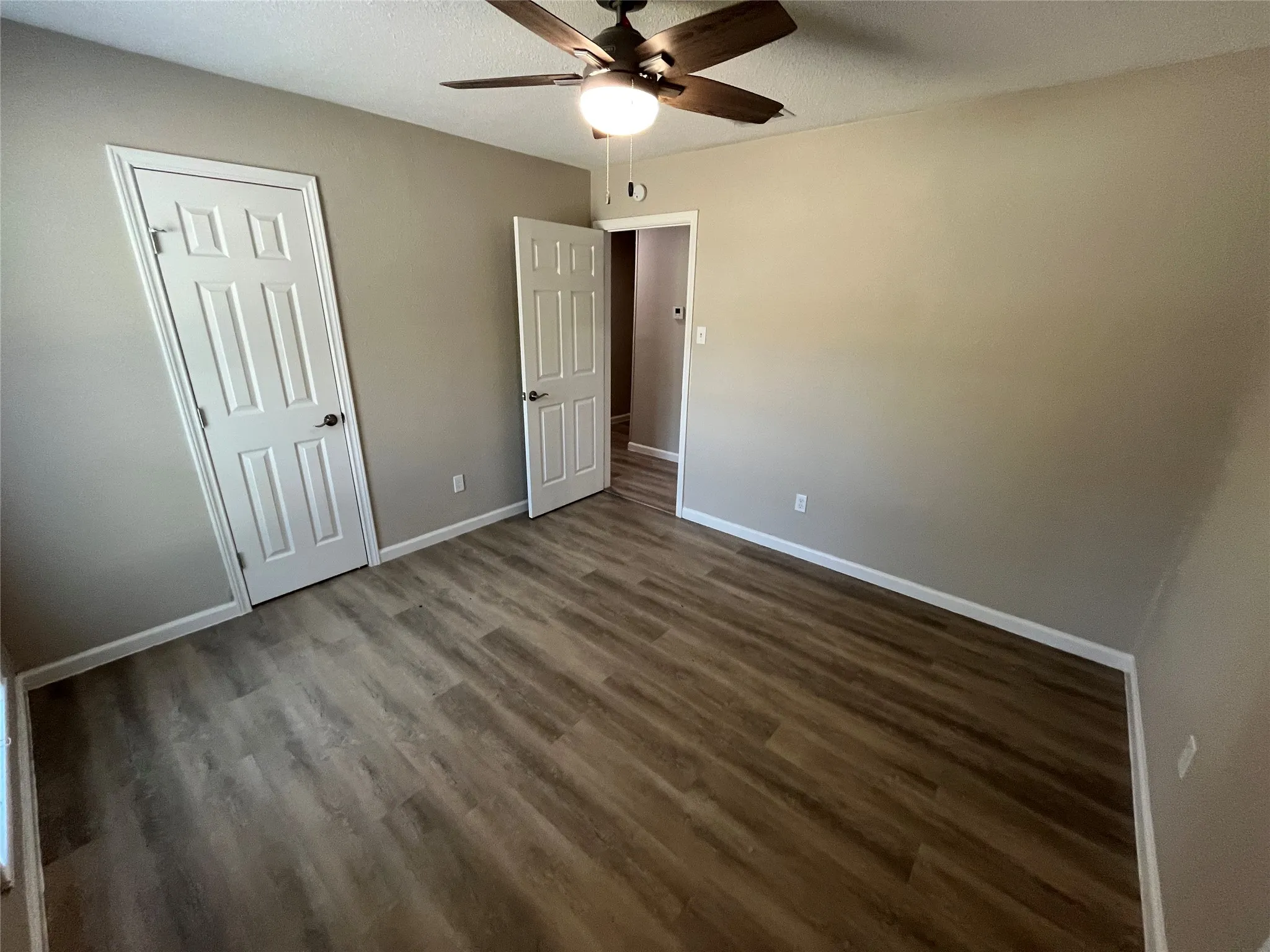 Wood-finish flooring, neutral wall tones, white paneled doors, and a ceiling fan with integrated lighting