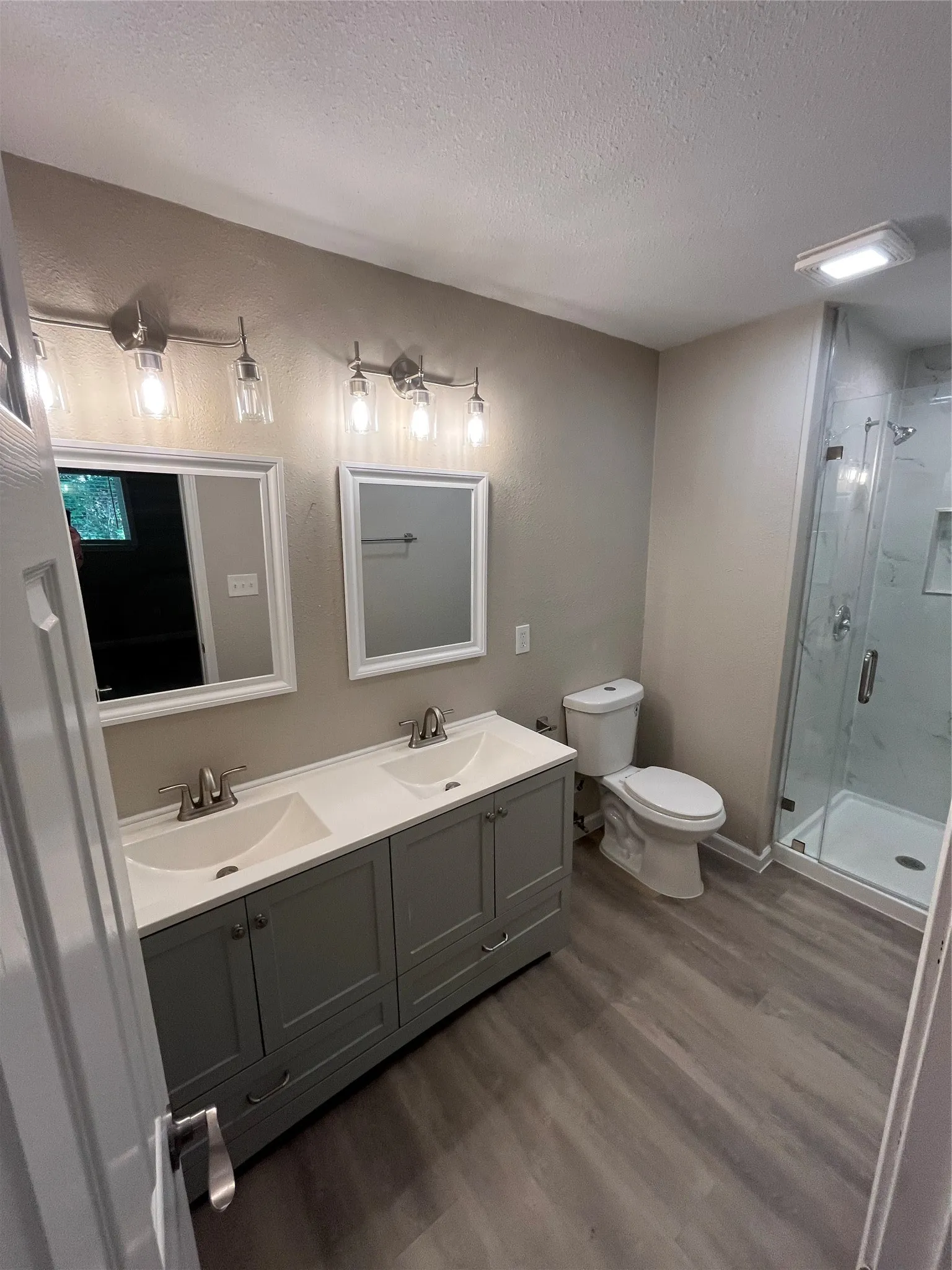 Dual vanity with integrated sinks, brushed nickel fixtures, wood-finish flooring, and a glass-enclosed shower