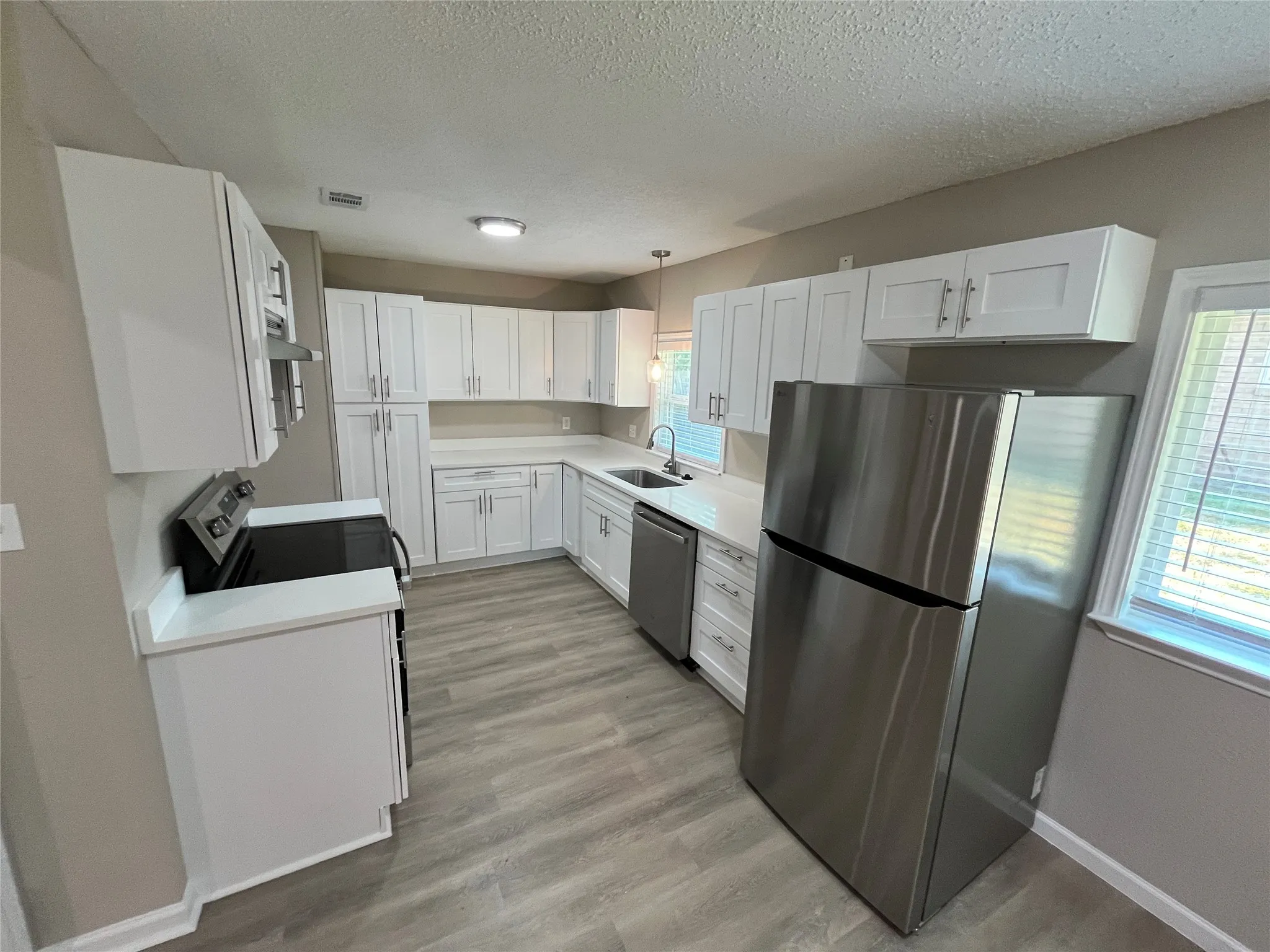 Kitchen featuring white shaker cabinetry, light-toned countertops, stainless steel appliances, and wood-finish flooring