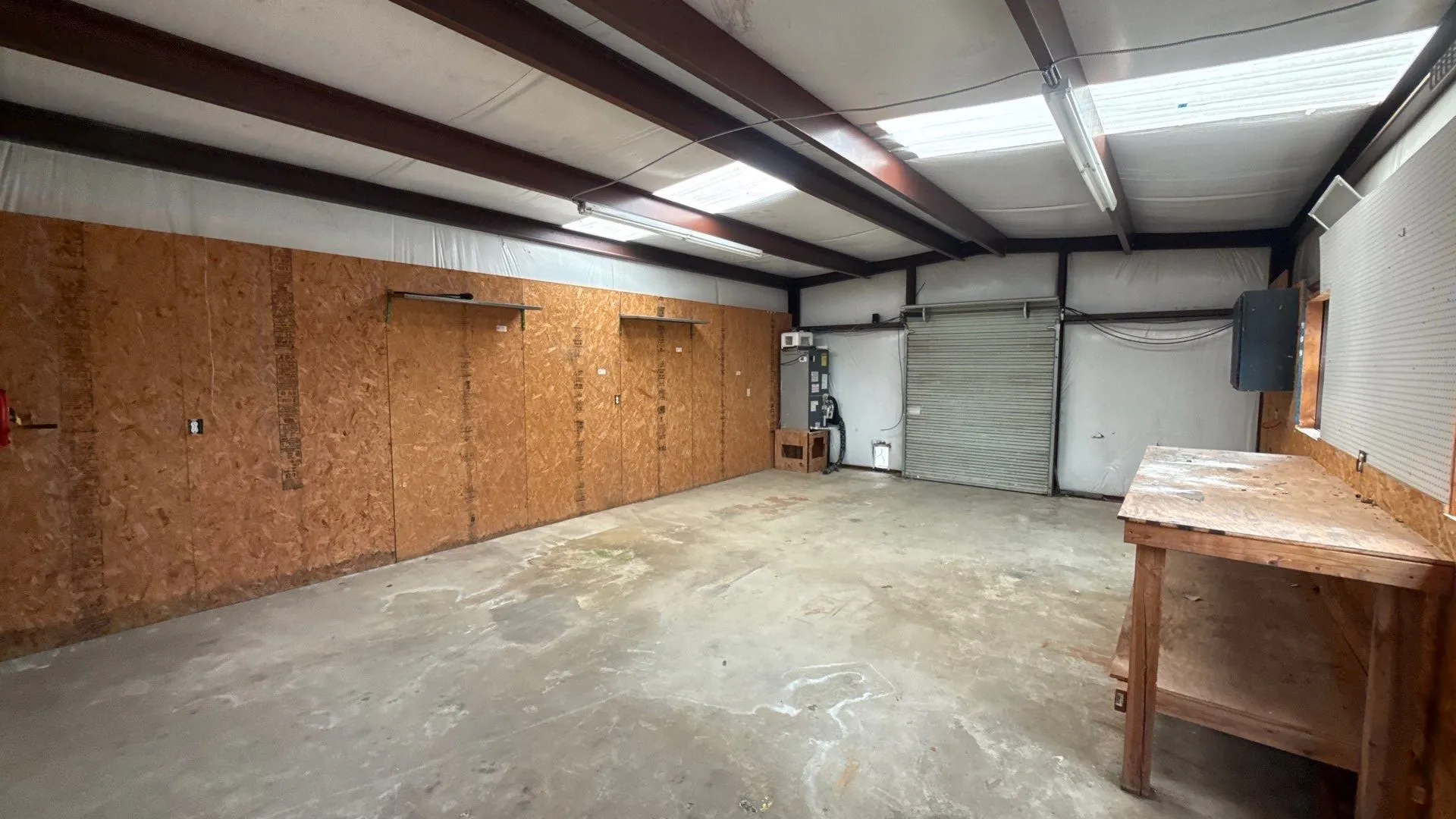 Concrete flooring, exposed metal beam ceiling, translucent ceiling panels, built-in workbench, and roll-up door