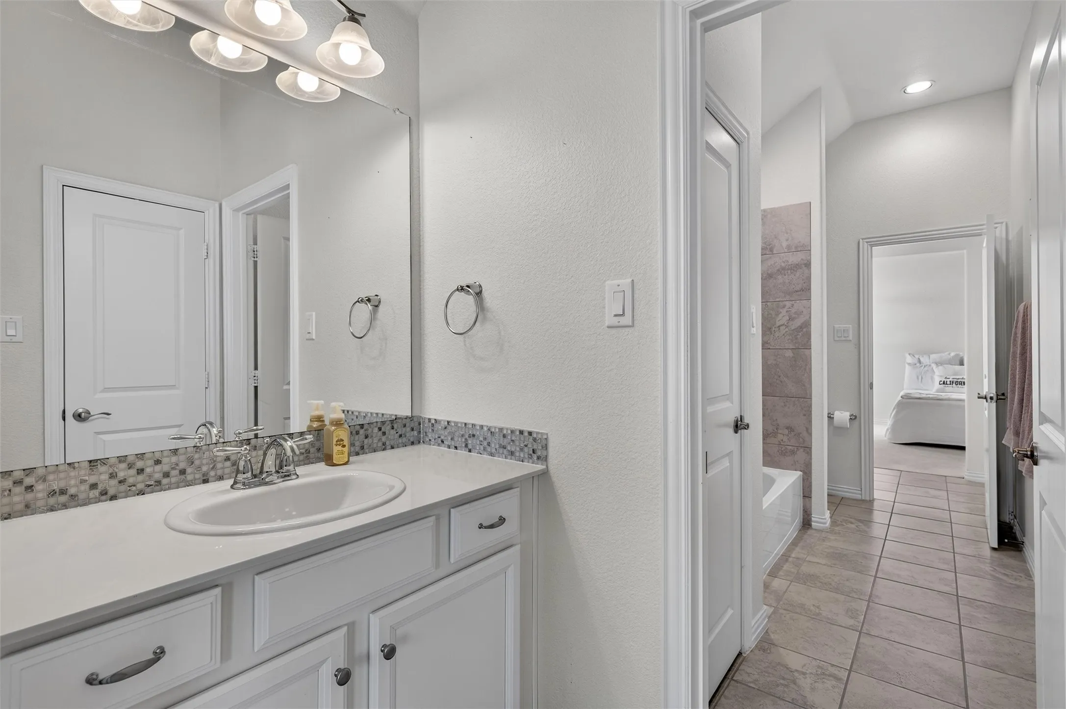 Bathroom vanity with white cabinetry, a single basin sink, and a multi-toned mosaic tile backsplash