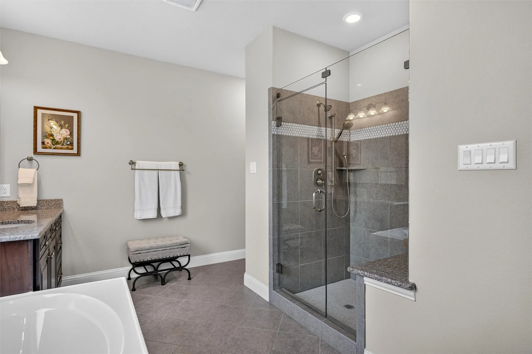 Glass-enclosed shower with tile surround and integrated shelving, complemented by a separate soaking tub and a vanity featuring a granite countertop