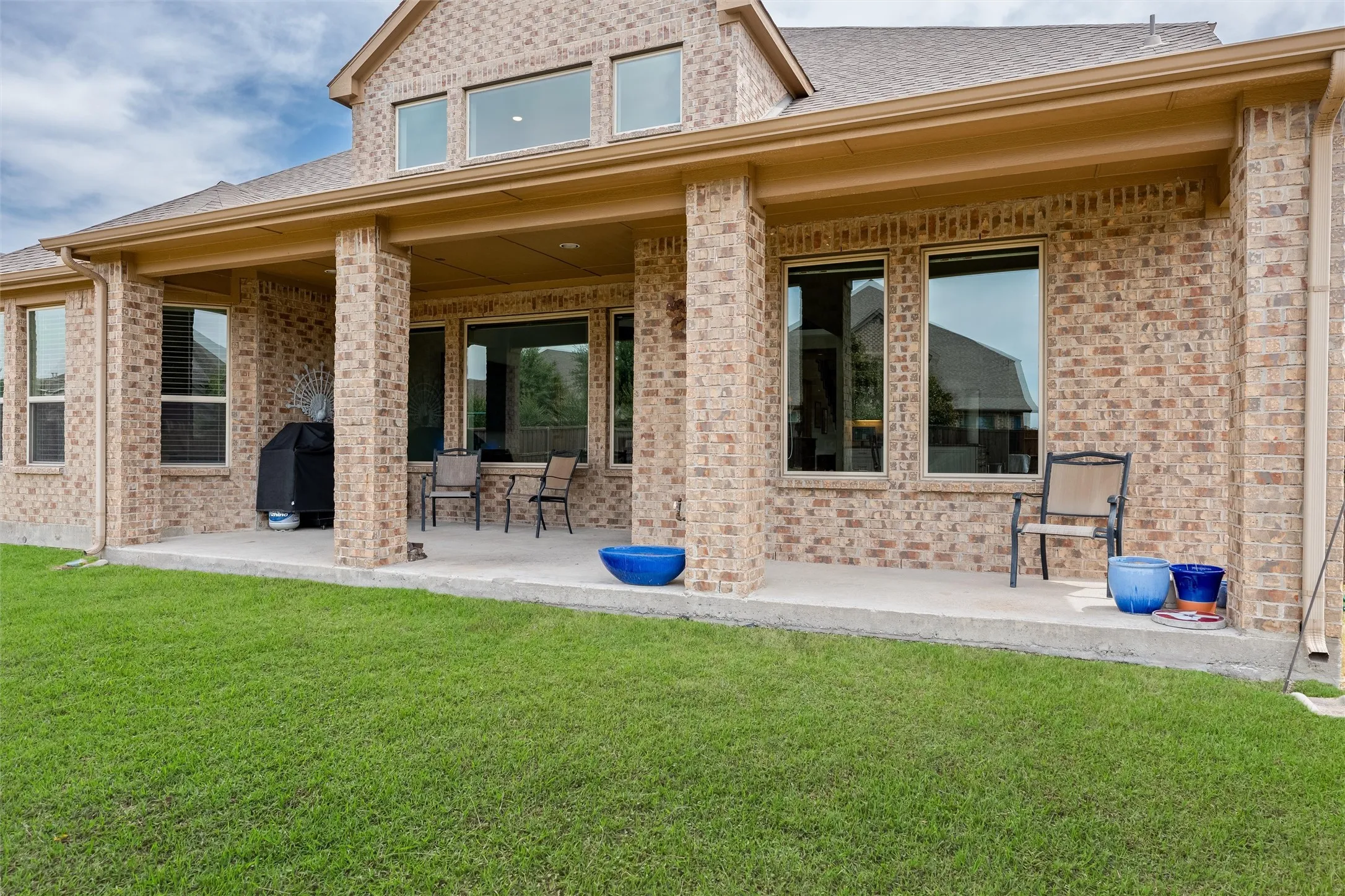 Brick exterior with a covered patio, multiple large windows, and a generous grassy area