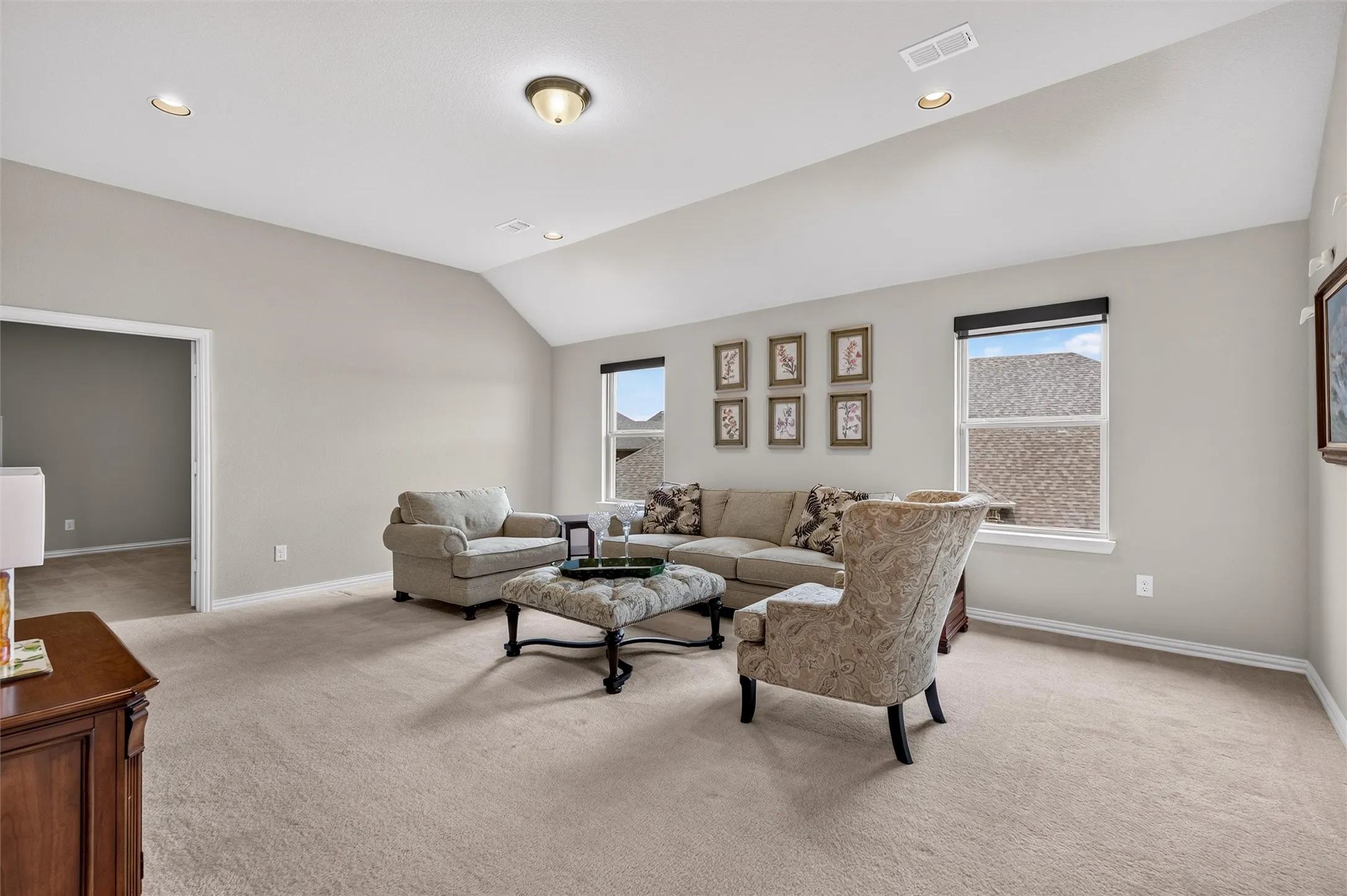 Vaulted ceiling with recessed lighting and a central flush-mount fixture, complemented by light neutral wall tones and carpet flooring