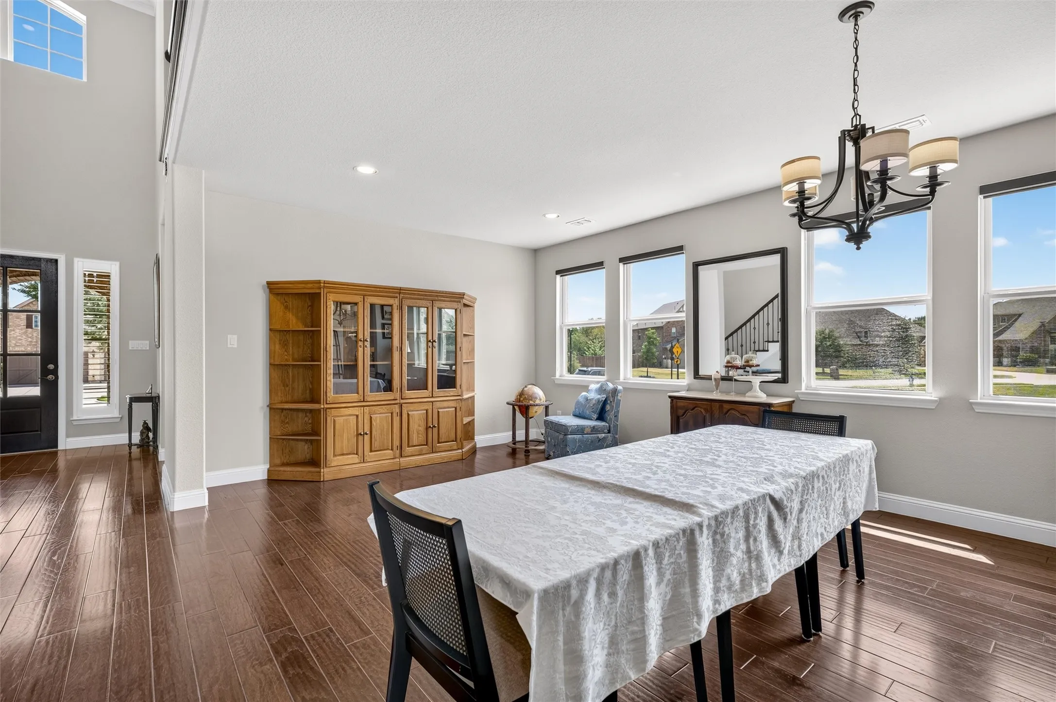 Hardwood-finish flooring throughout, multiple windows, high ceilings, a prominent chandelier, and a black front door with decorative glass