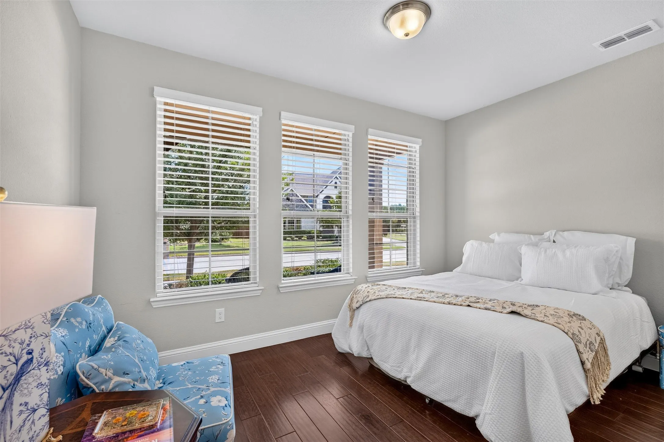 Wood-finish flooring, three windows with white blinds, light gray wall paint, and a semi-flush mount ceiling light fixture