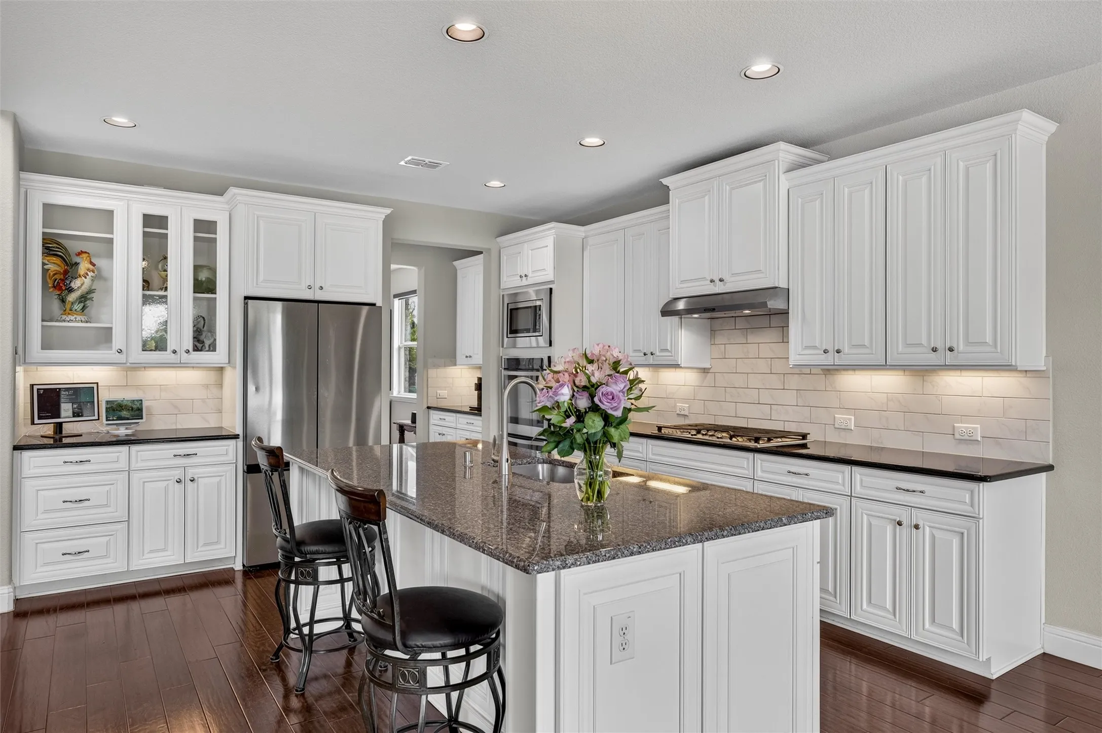 Kitchen featuring white cabinetry, a center island with a stone countertop, dark wood-finish flooring, stainless steel appliances, and a subway tile backsplash