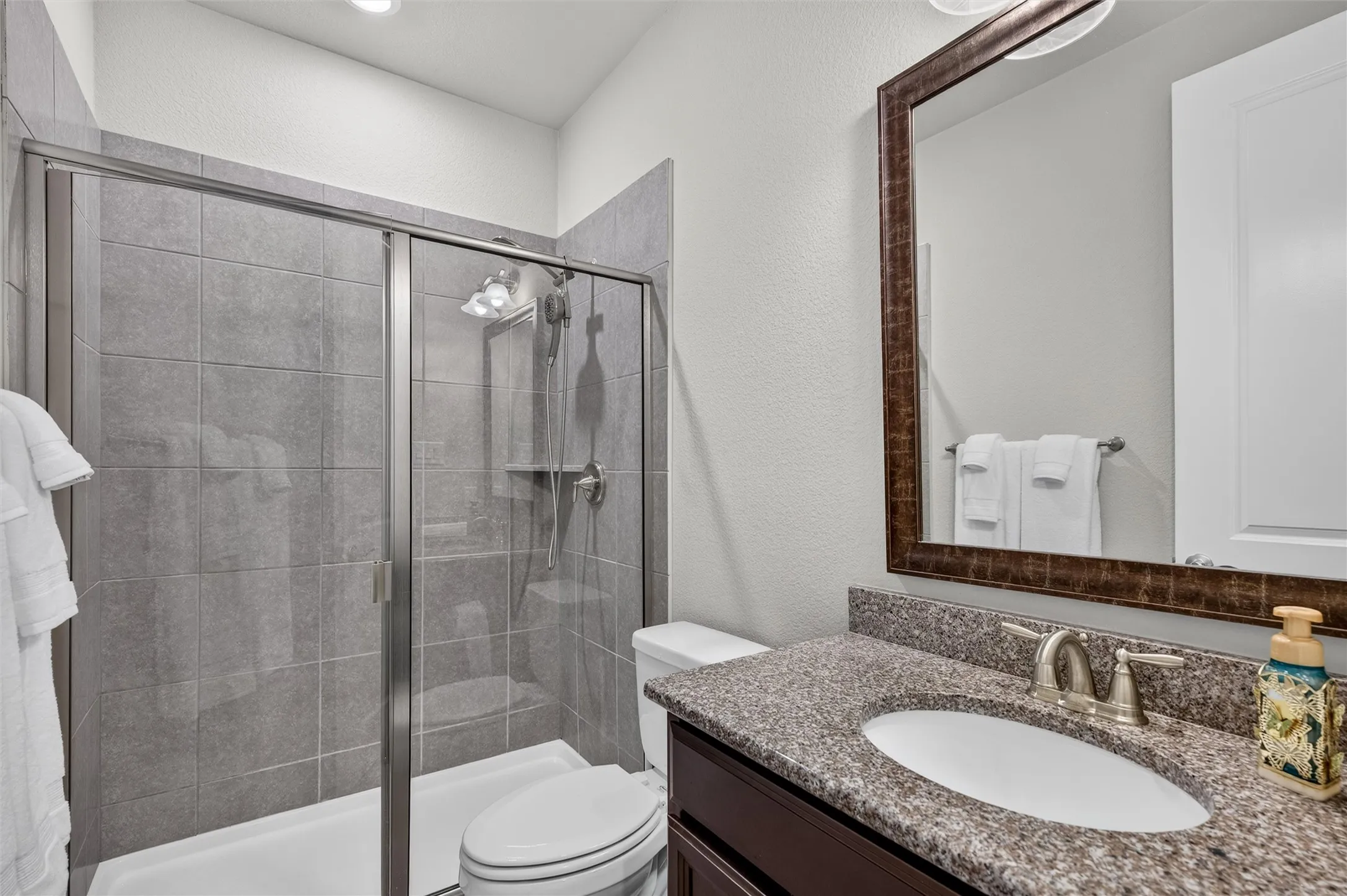 Shower enclosure with sliding glass doors, gray tiled walls, and a built-in shelf