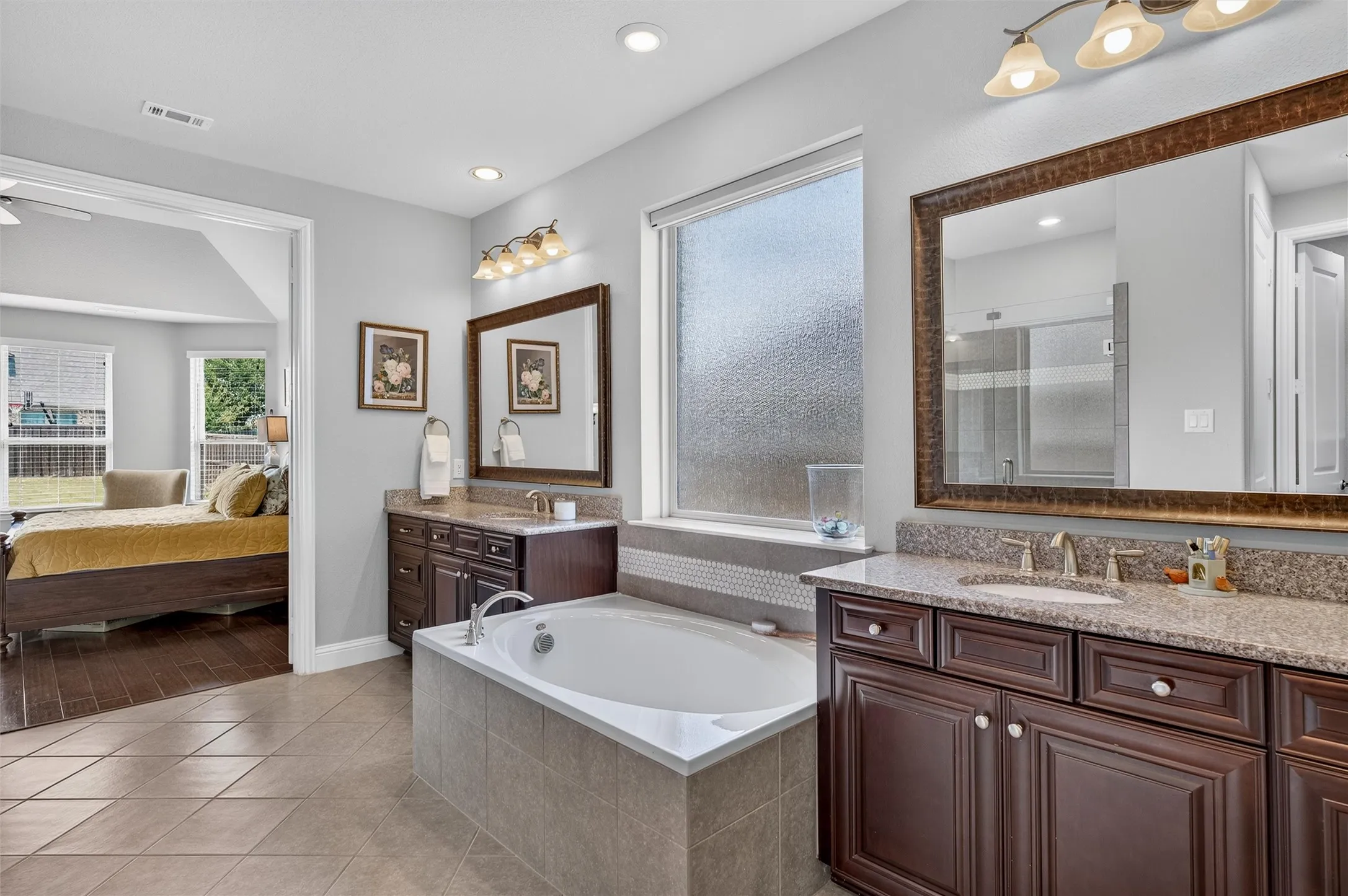Dual vanities with granite countertops, a built-in soaking tub, tile flooring, and recessed lighting