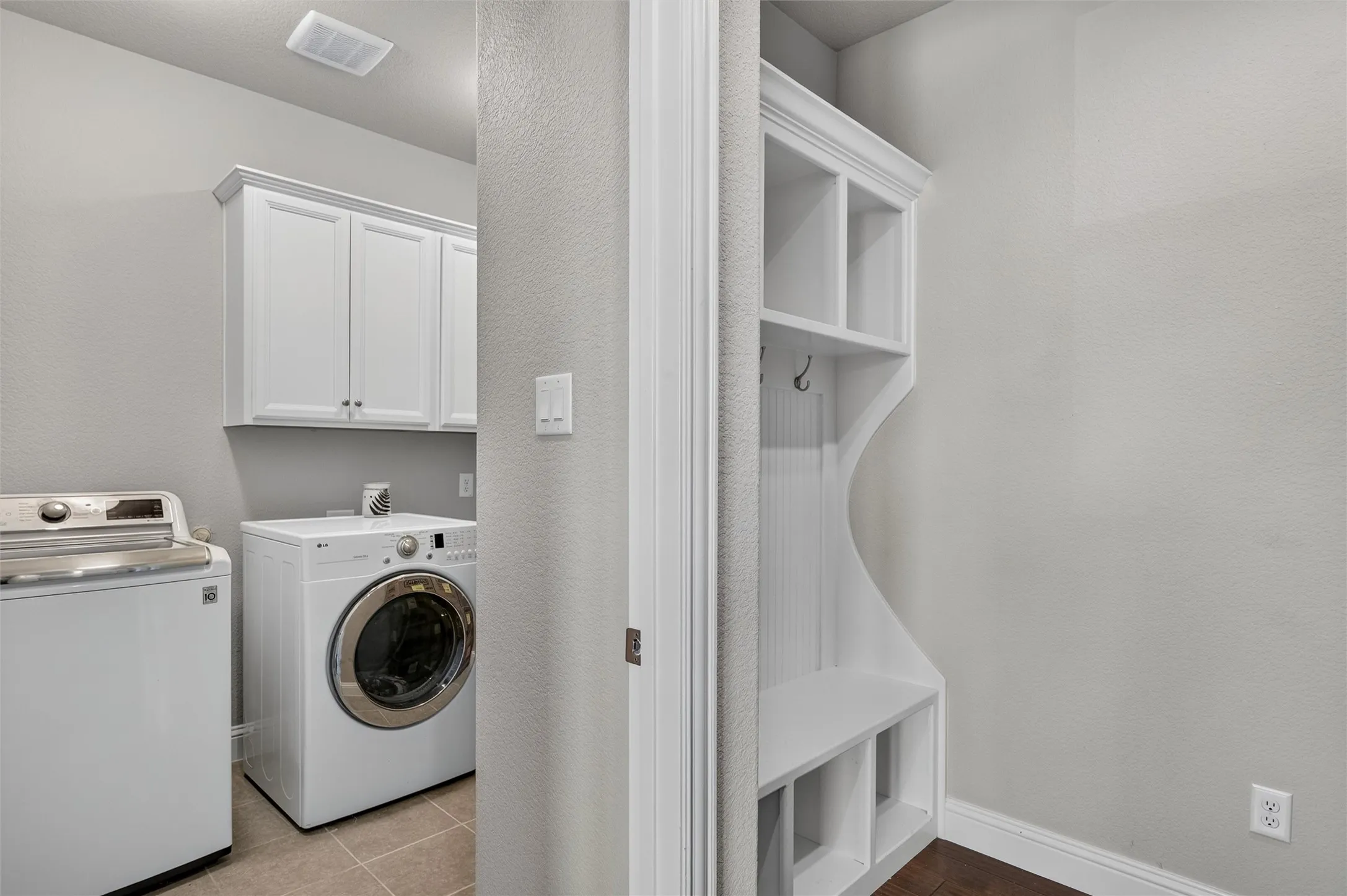White shaker-style cabinetry, built-in storage bench with cubbies, tile flooring, and wood-finish flooring