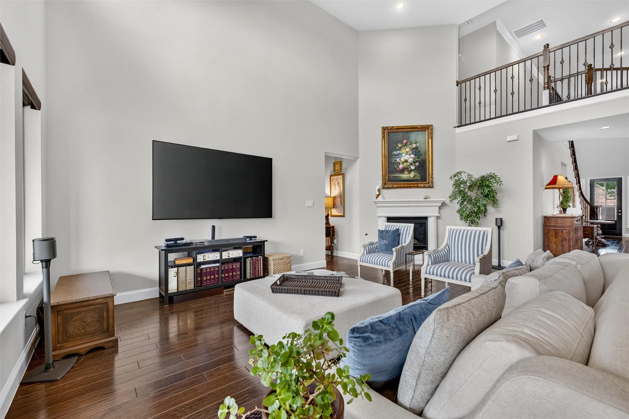 Soaring ceiling with recessed lighting, rich wood-finish flooring, and a fireplace with a decorative mantel