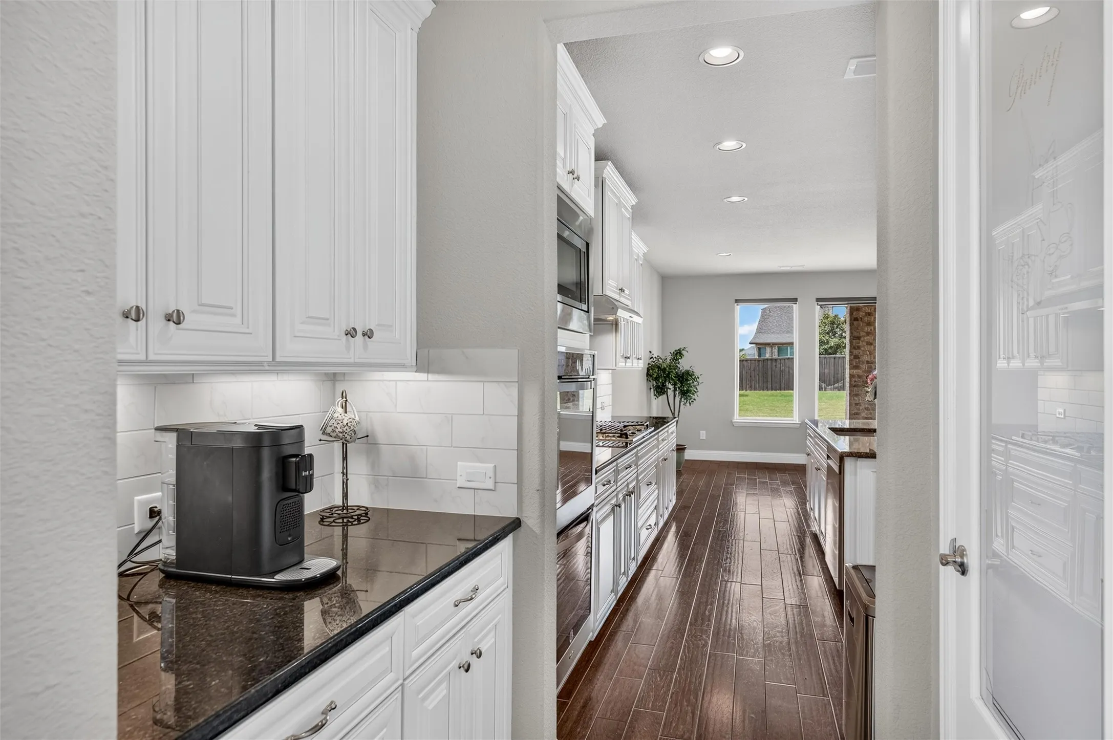 Kitchen area featuring white cabinetry, dark countertops, a white subway tile backsplash, and wood-finish flooring