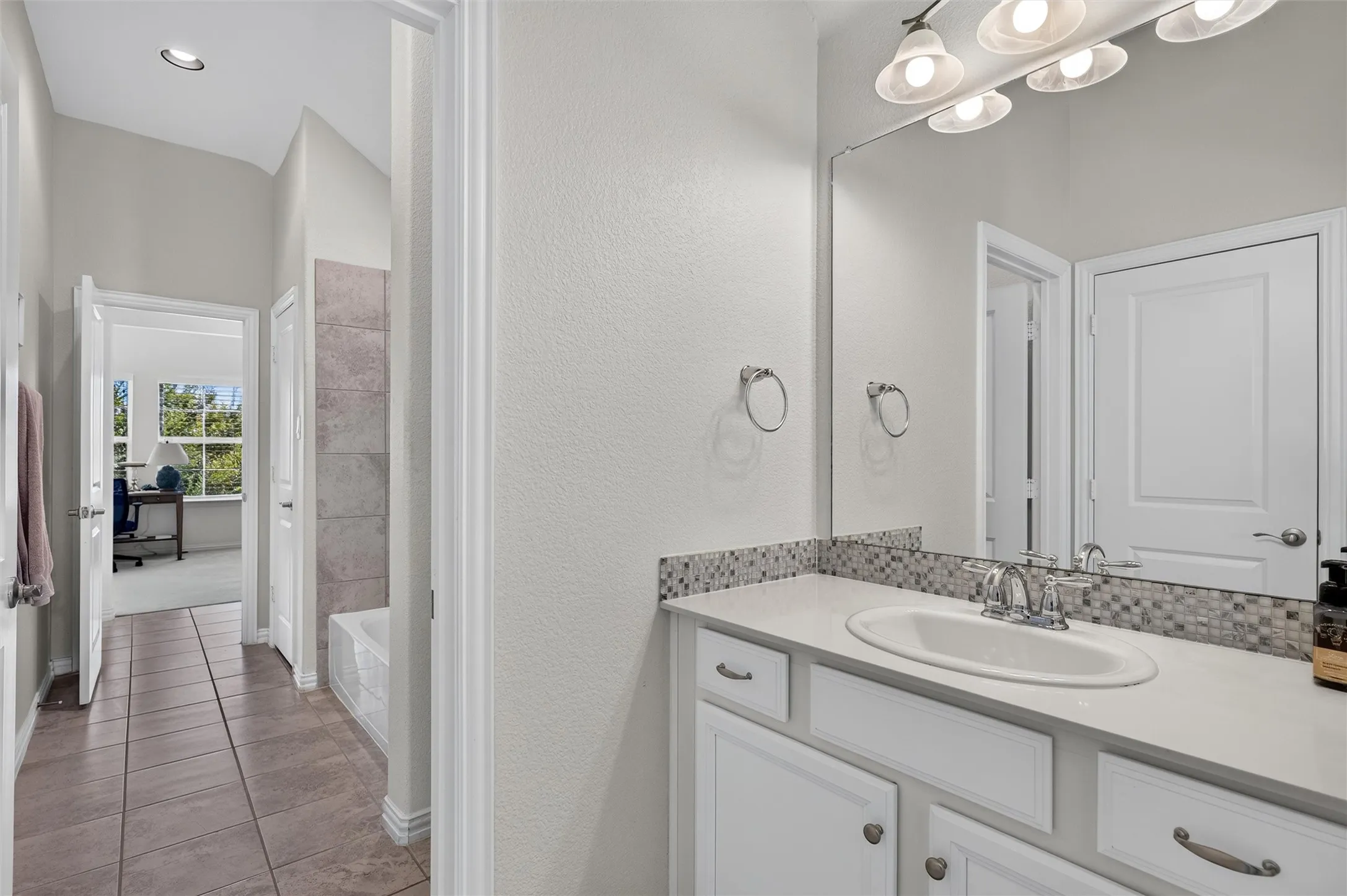Vanity with an oval undermount sink, mosaic tile backsplash, and polished chrome faucet