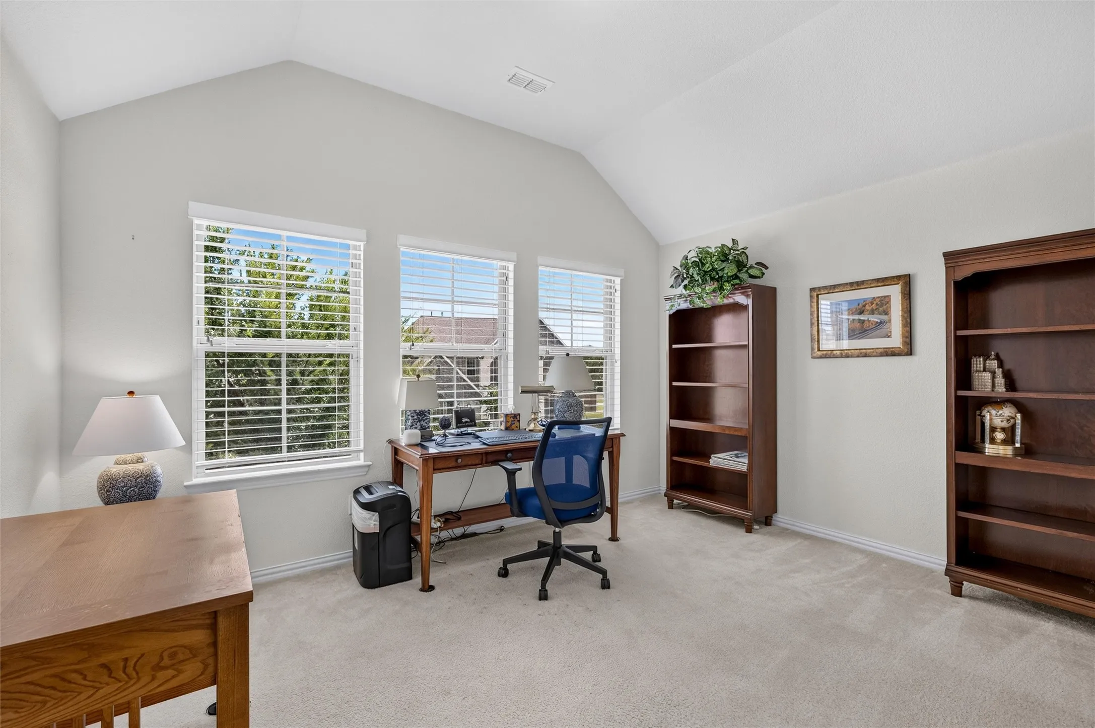 Room featuring a vaulted ceiling, light-colored carpeting, and multiple windows with blinds