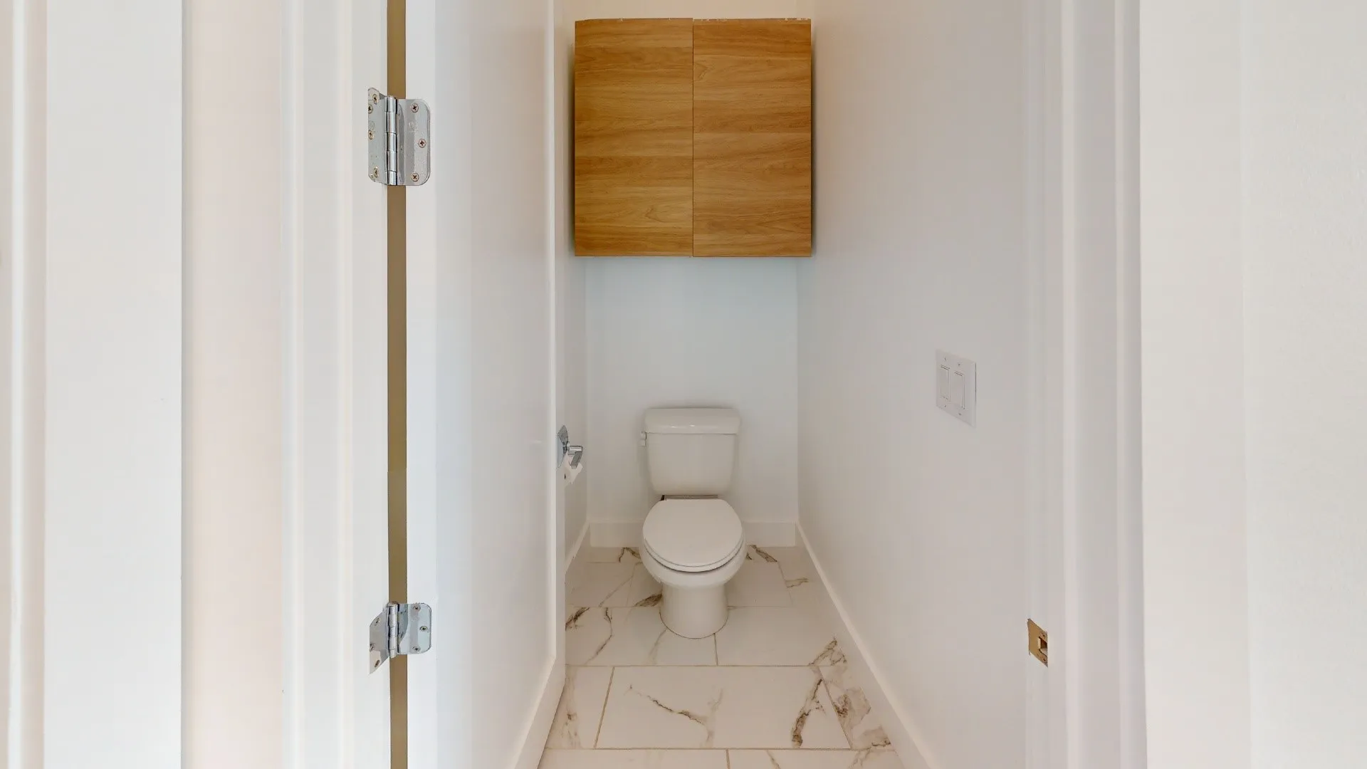 Recessed toilet with wood-finish wall-mounted cabinetry and white tile flooring