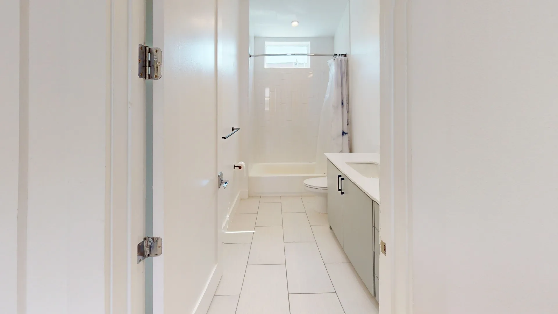 White tiled flooring, light gray vanity, white countertop, built-in bathtub, and horizontal window
