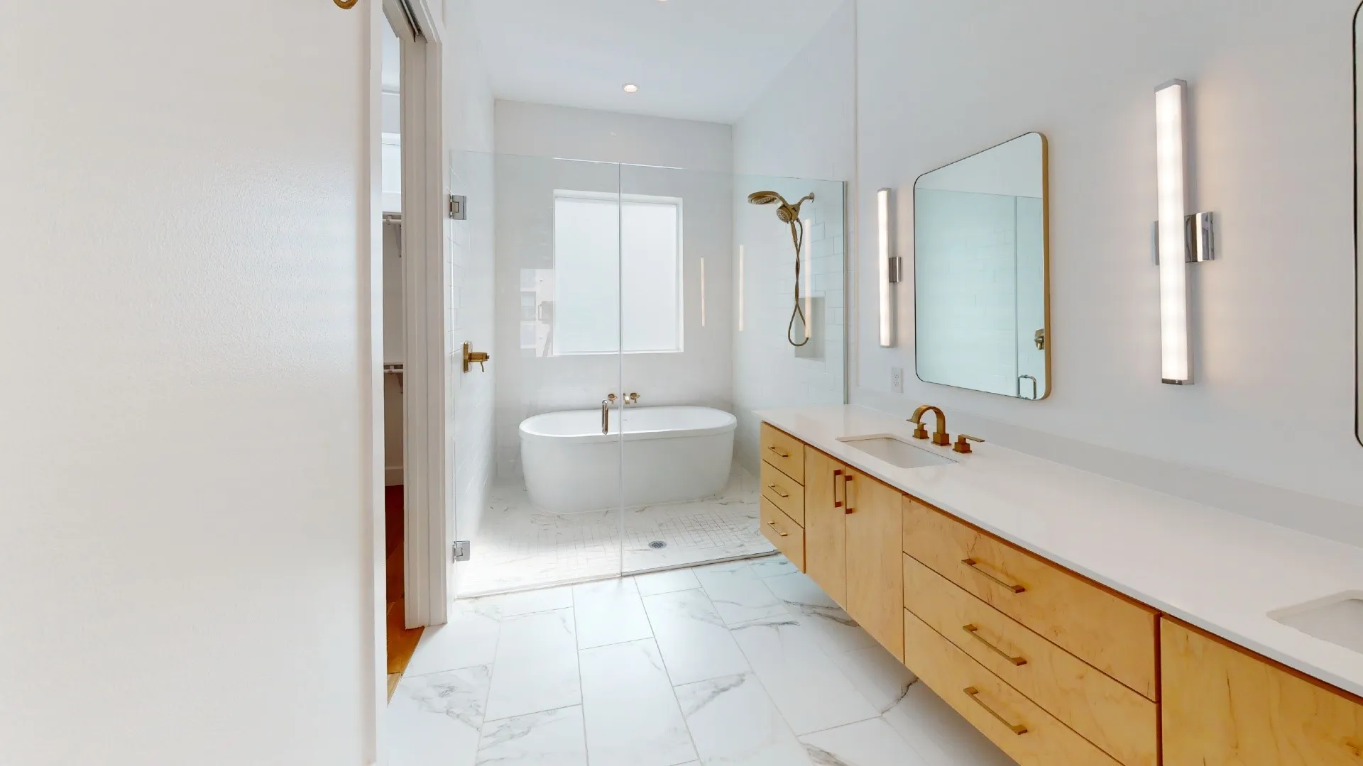 Freestanding soaking tub, frameless glass shower enclosure, dual vanity with undermount sinks, wood-finish cabinetry, and large format floor tiling