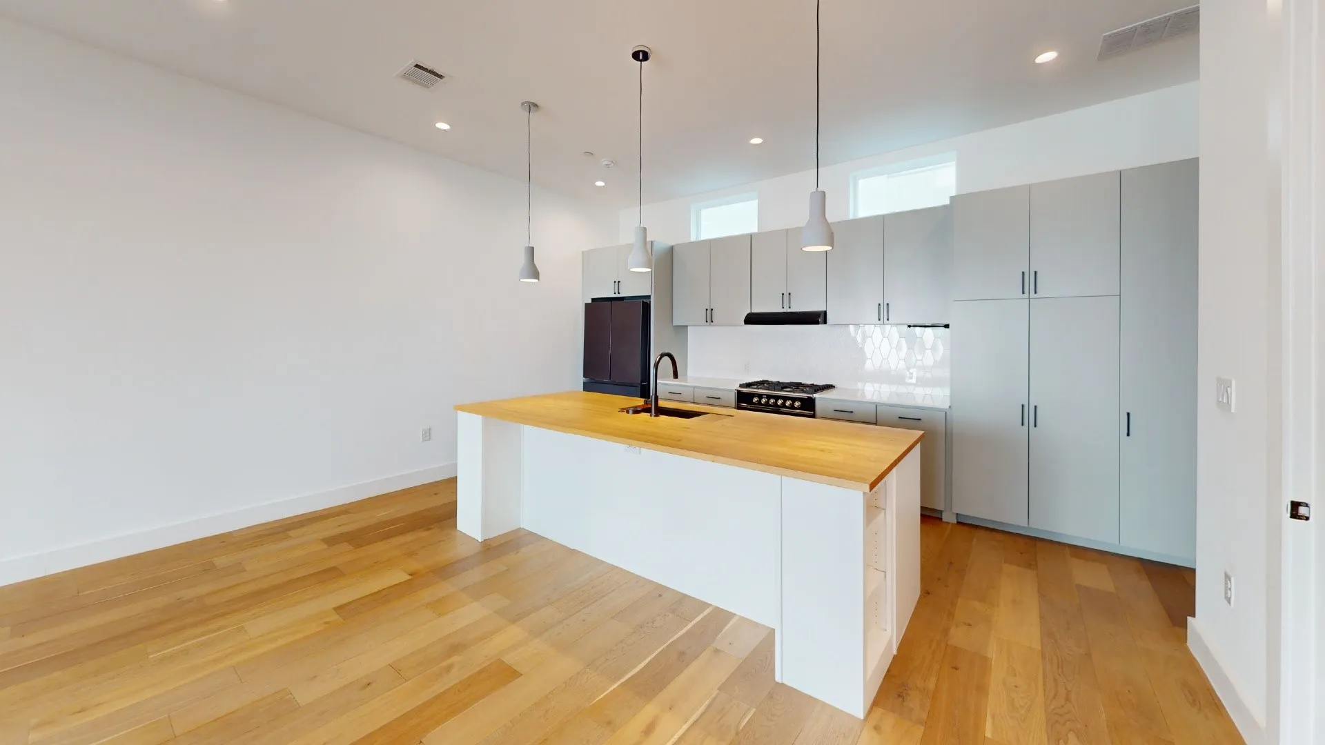 Hardwood flooring, kitchen island with wood-finish countertop, pendant lighting, stainless steel range with black hood, and full-height cabinetry