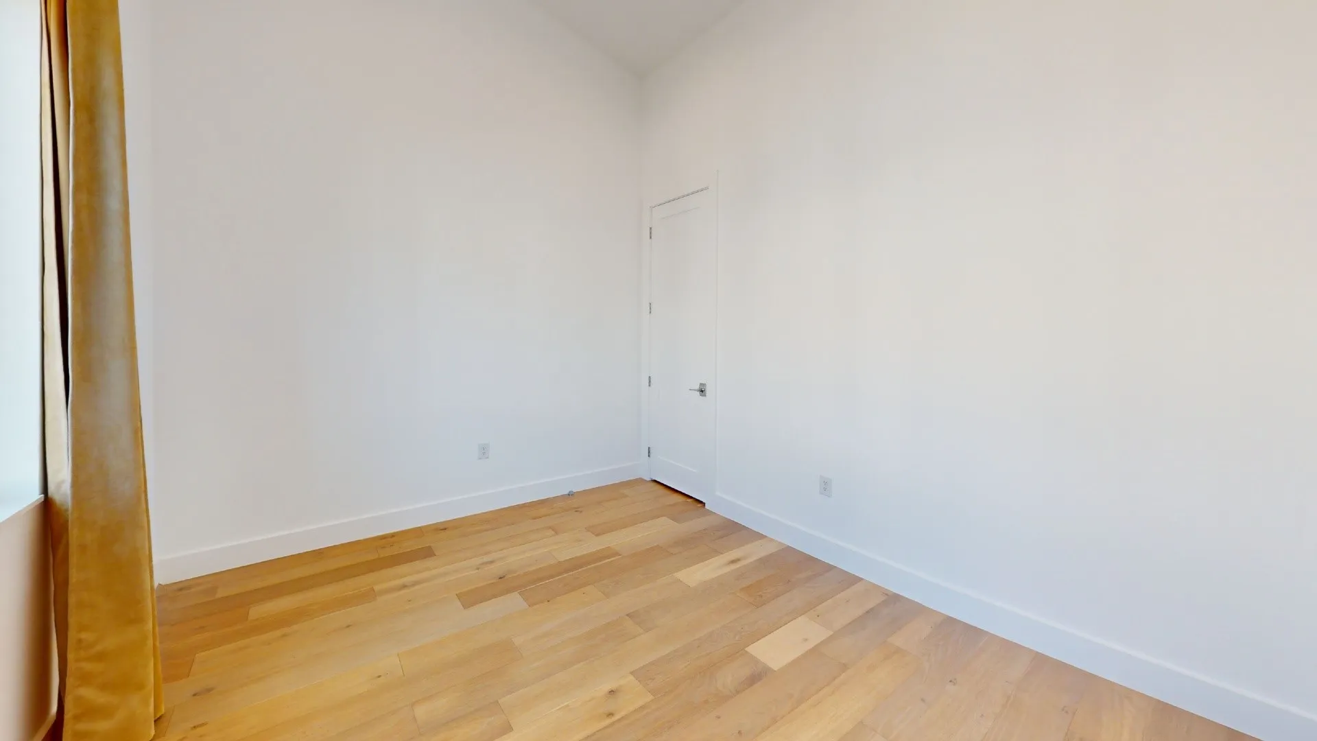 Hardwood flooring with white baseboards, white walls, and a white door with a silver handle