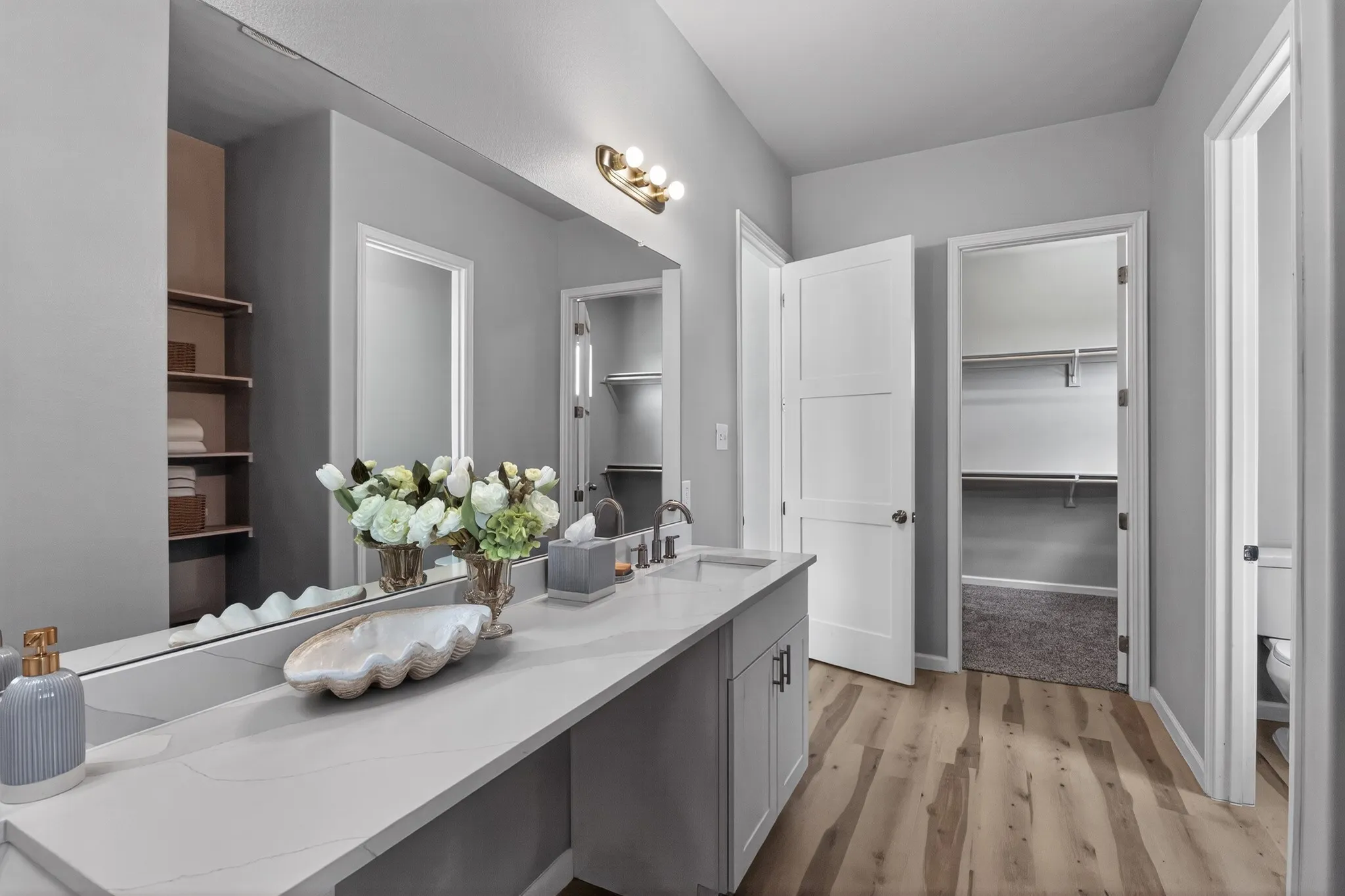 Dual vanity with quartz countertop, wood-finish flooring, built-in shelving, two interior doors, and modern light fixtures