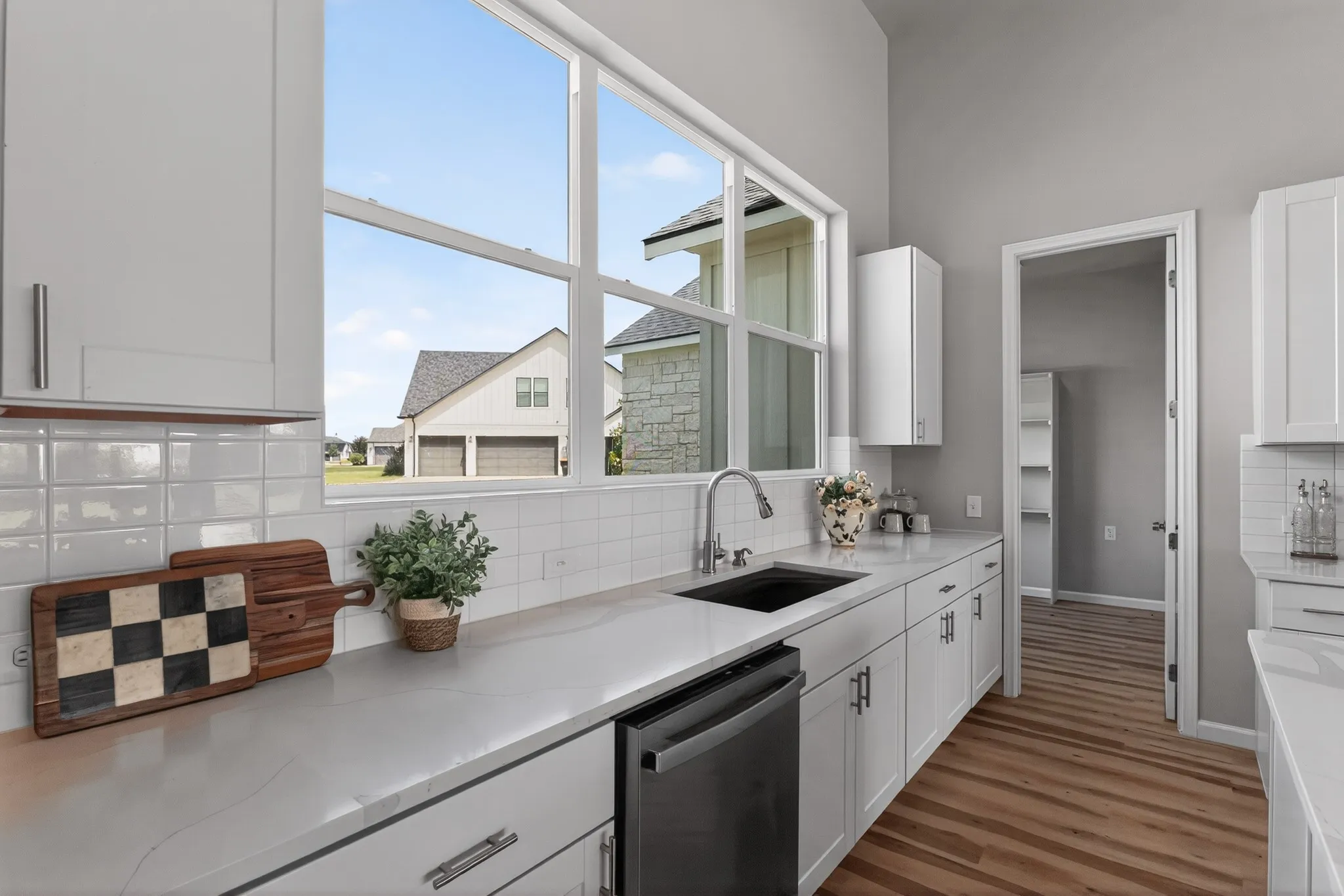 Kitchen featuring a large window, white cabinetry with modern hardware, a stainless steel sink, light-toned countertops, and wood-finish flooring