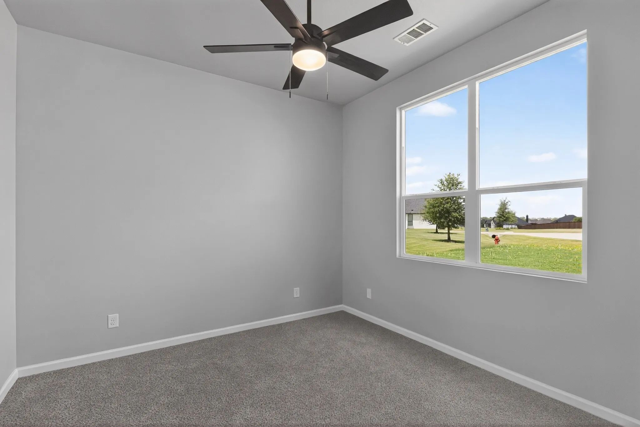 Bright room featuring a large window, plush gray carpeting, crisp white baseboards, and a modern ceiling fan with integrated lighting