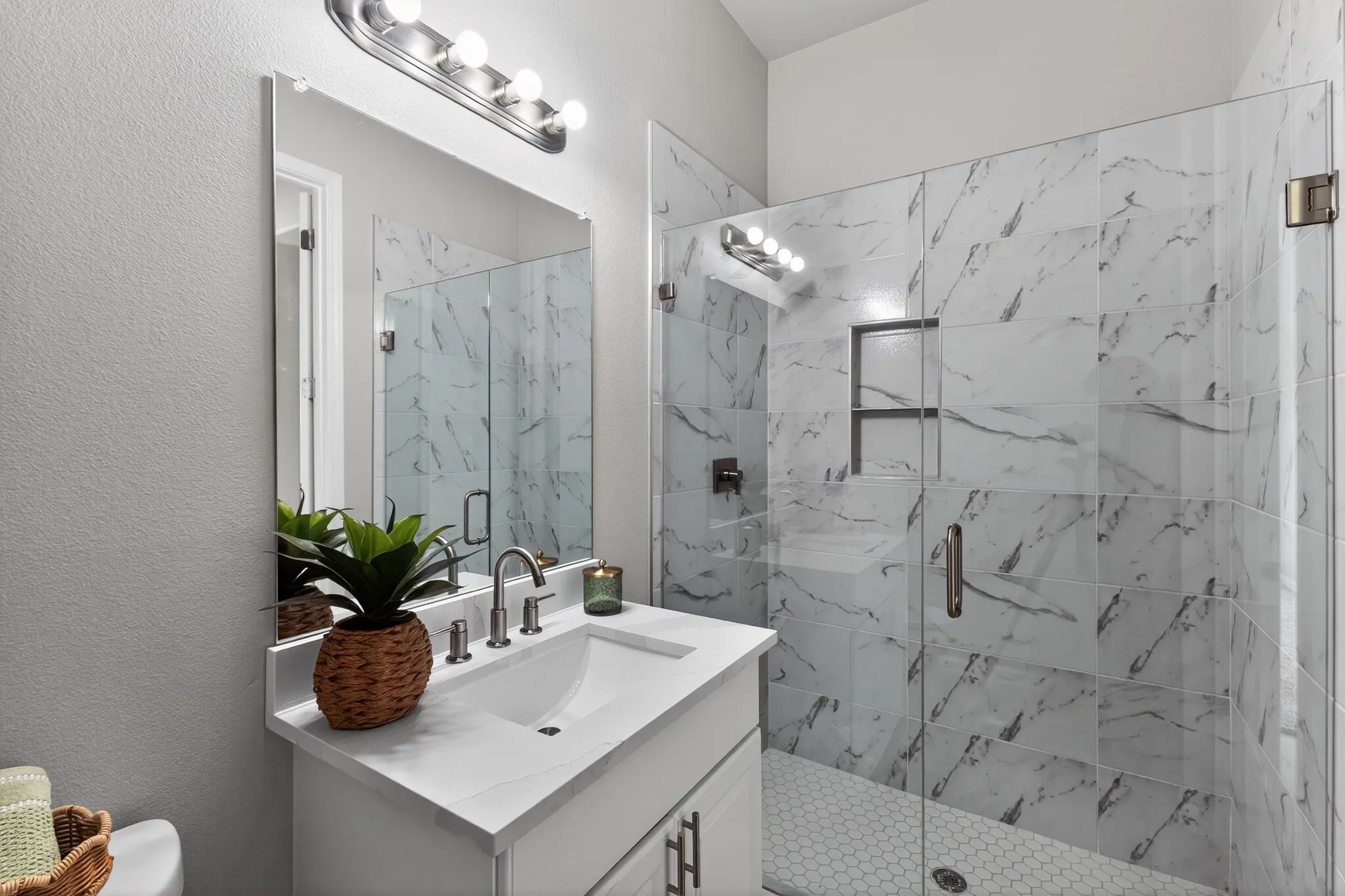Modern bathroom featuring a glass-enclosed shower with large format marble-look tile, a built-in shower niche, and a hex tile shower floor