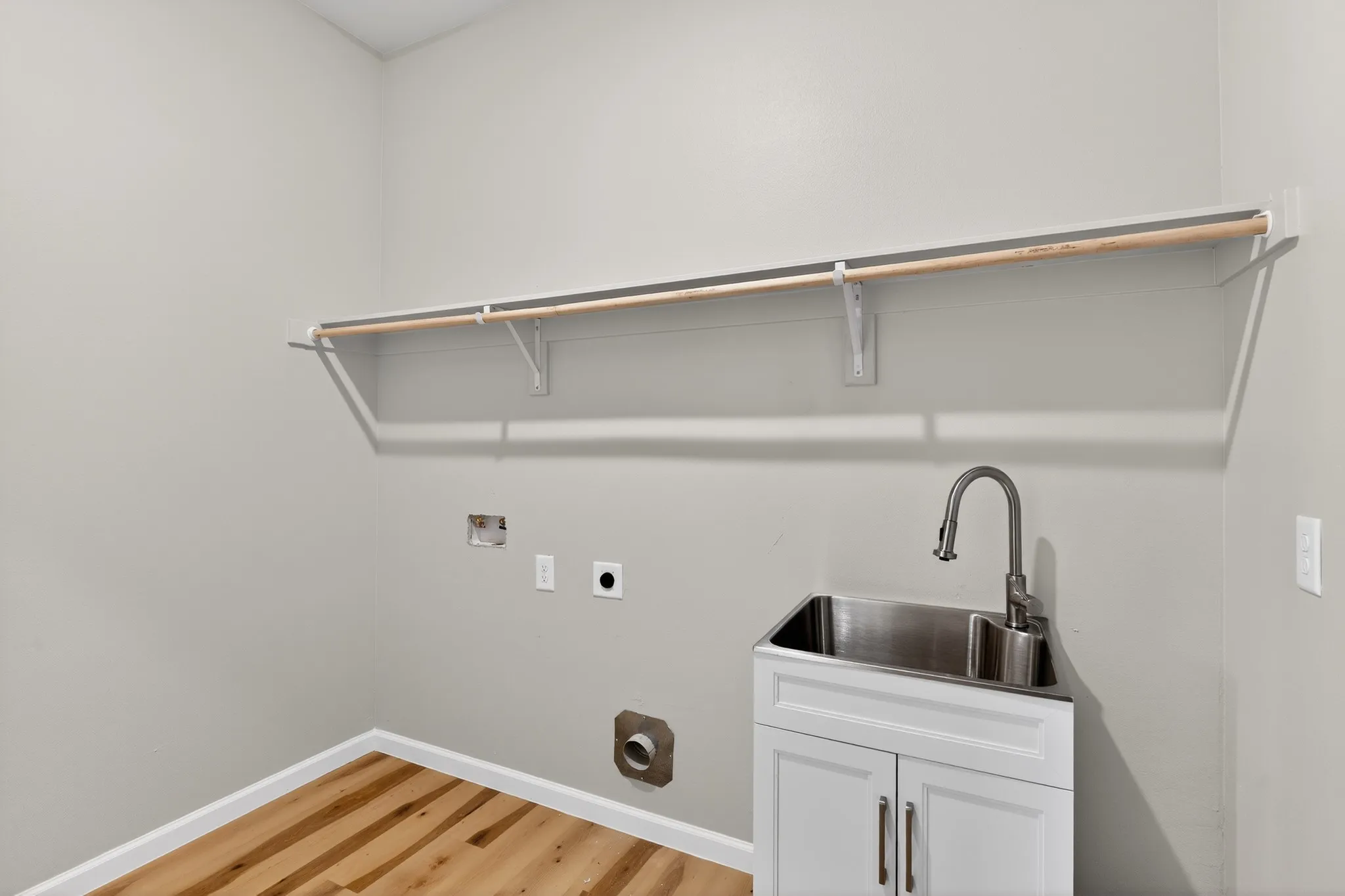 Laundry area featuring a utility sink with a brushed nickel pull-down faucet, a white base cabinet, and wood-finish flooring