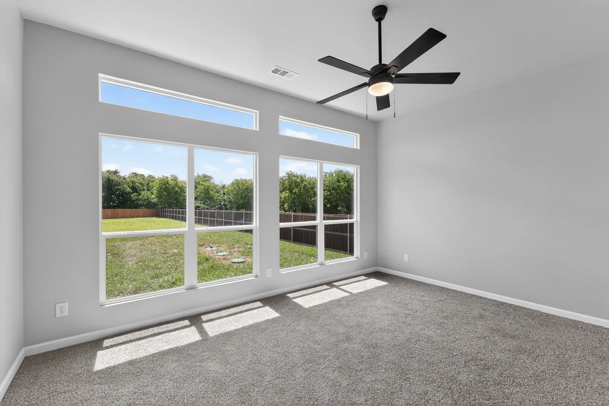 Room featuring a large window array with transom windows, a black ceiling fan with integrated lighting, and neutral-toned wall paint