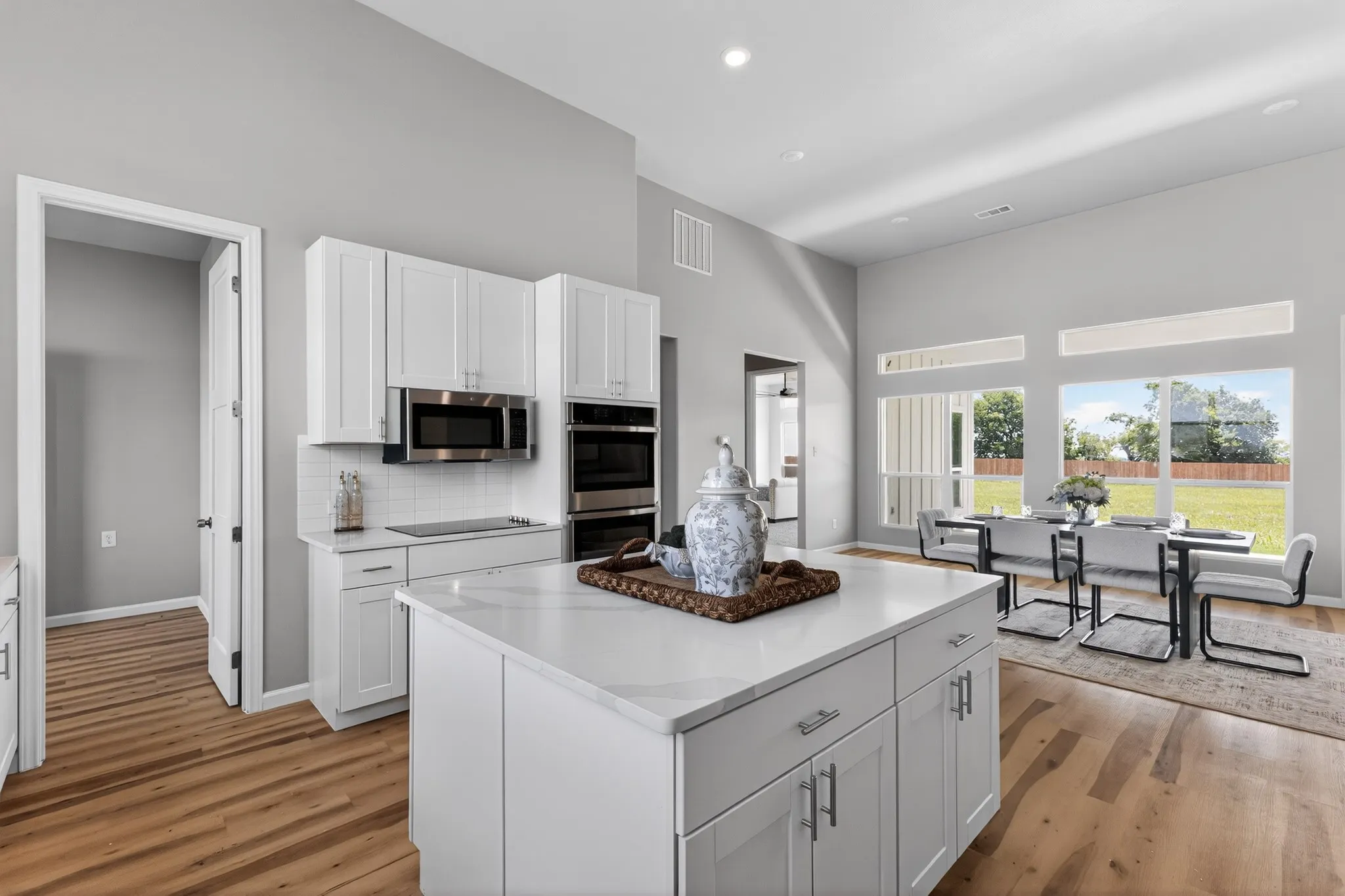 Open-concept kitchen and dining area featuring a spacious island with a quartz countertop, white shaker cabinetry, stainless steel appliances, and wood-finish flooring