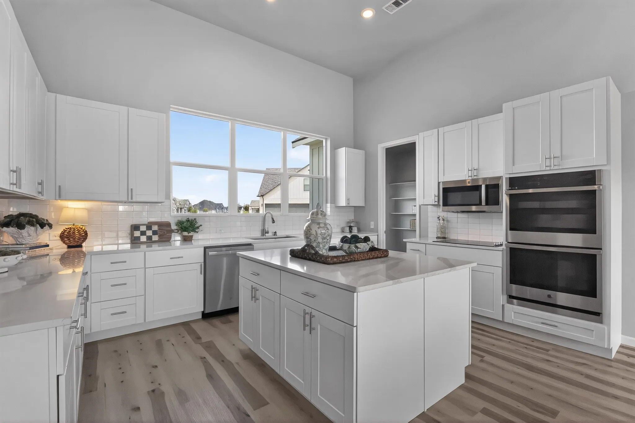 Modern kitchen featuring a central island, white cabinetry, integrated stainless steel appliances, light wood-finish flooring, and a large window