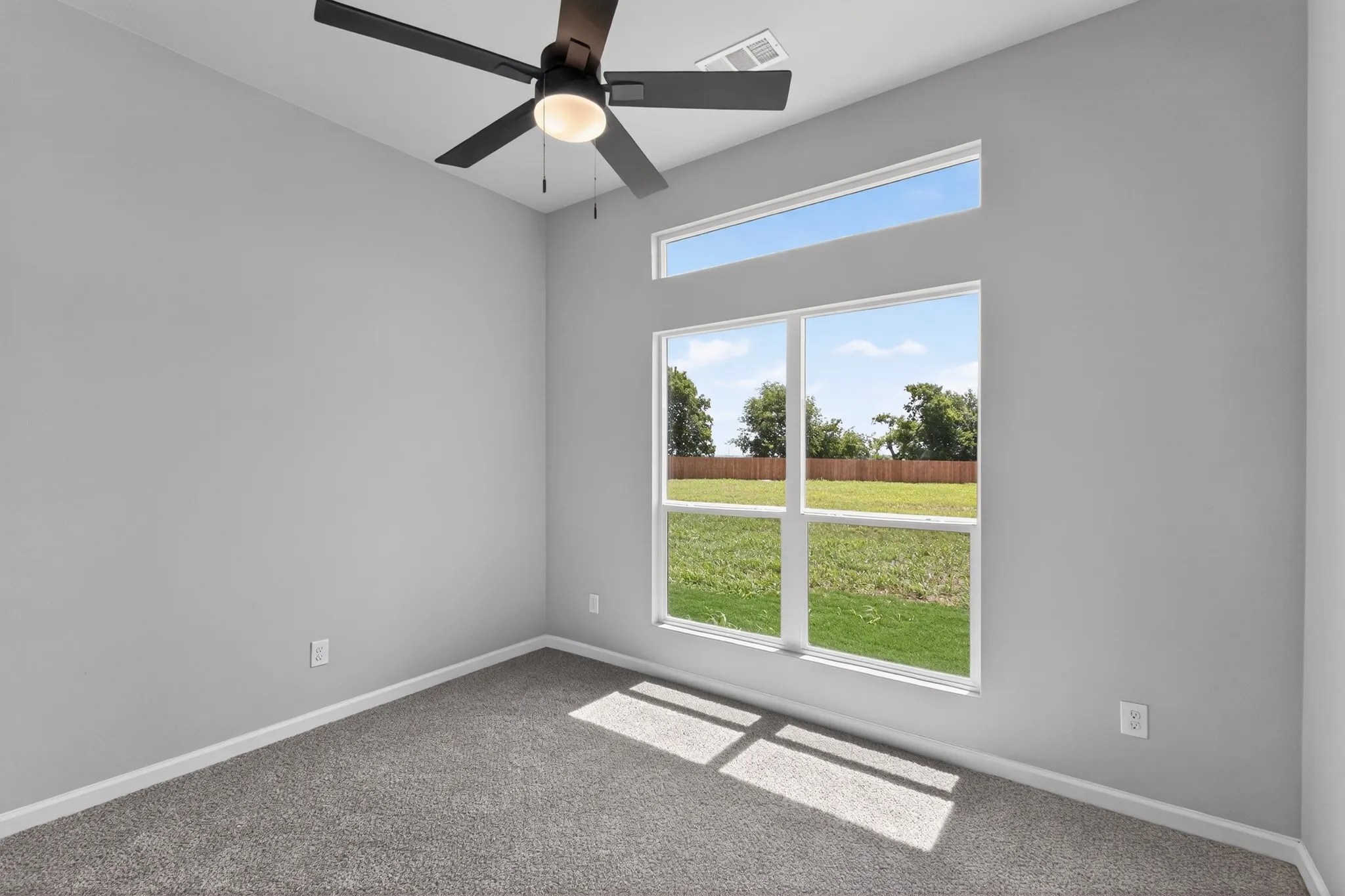 Room featuring light gray walls, gray carpet, a contemporary ceiling fan with light fixture, and a large multi-pane window with a transom