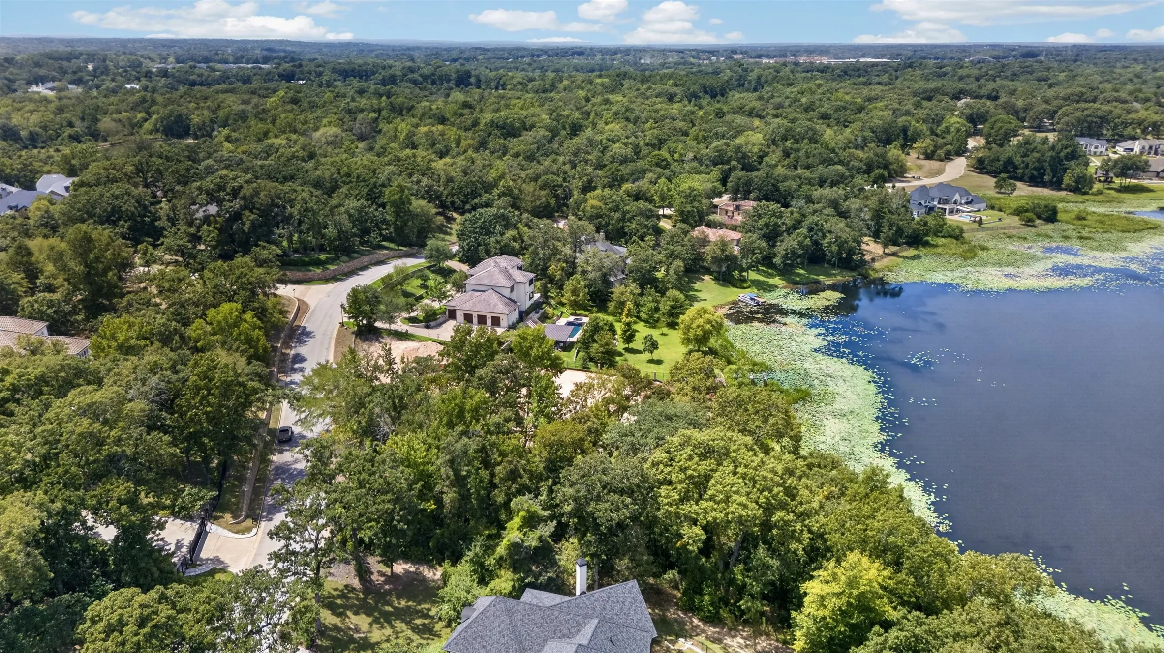 Expansive treed landscape featuring a lake, residential properties, and a winding road
