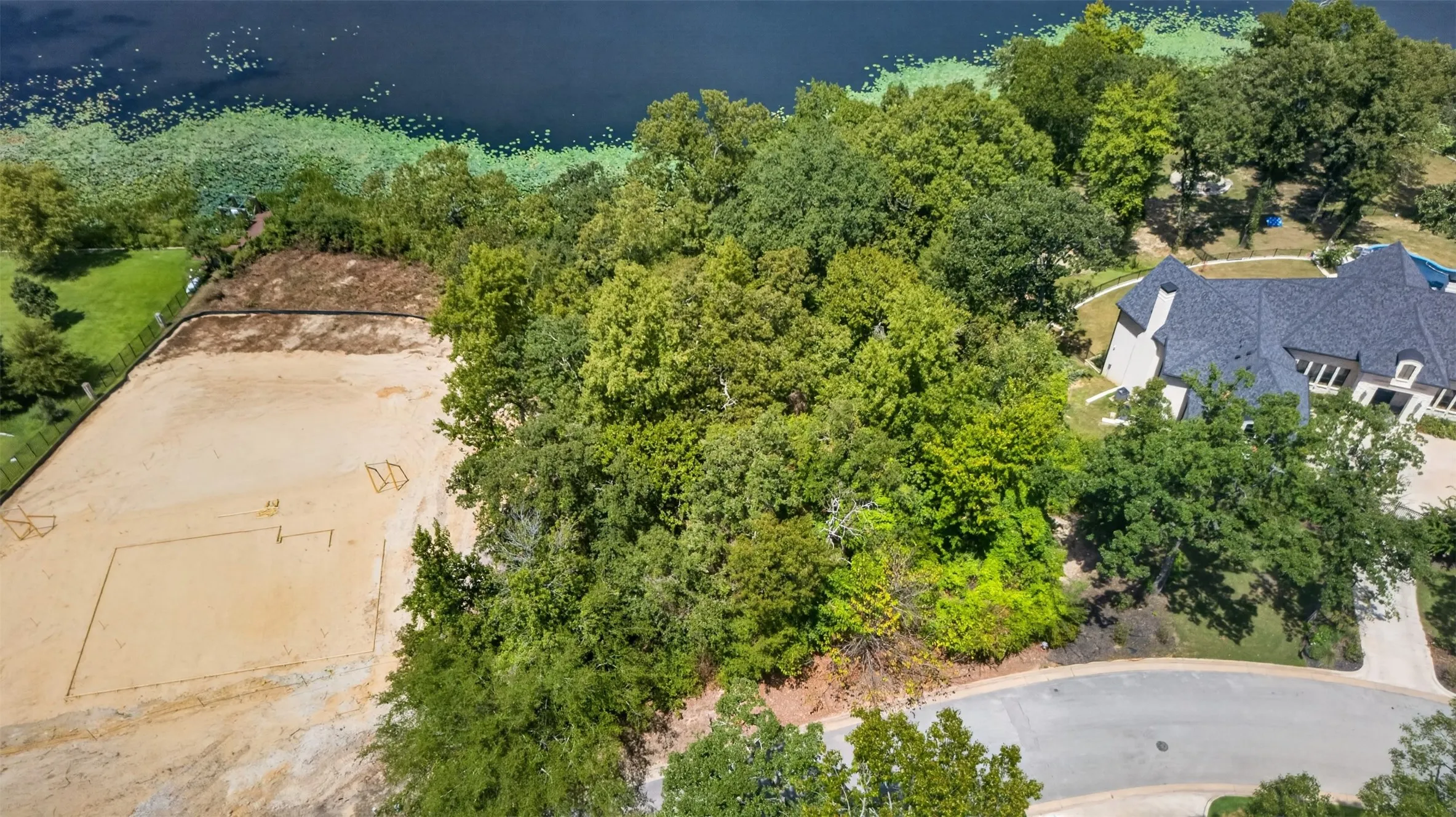 Expansive land parcel featuring mature trees, a sand court, and a paved street frontage