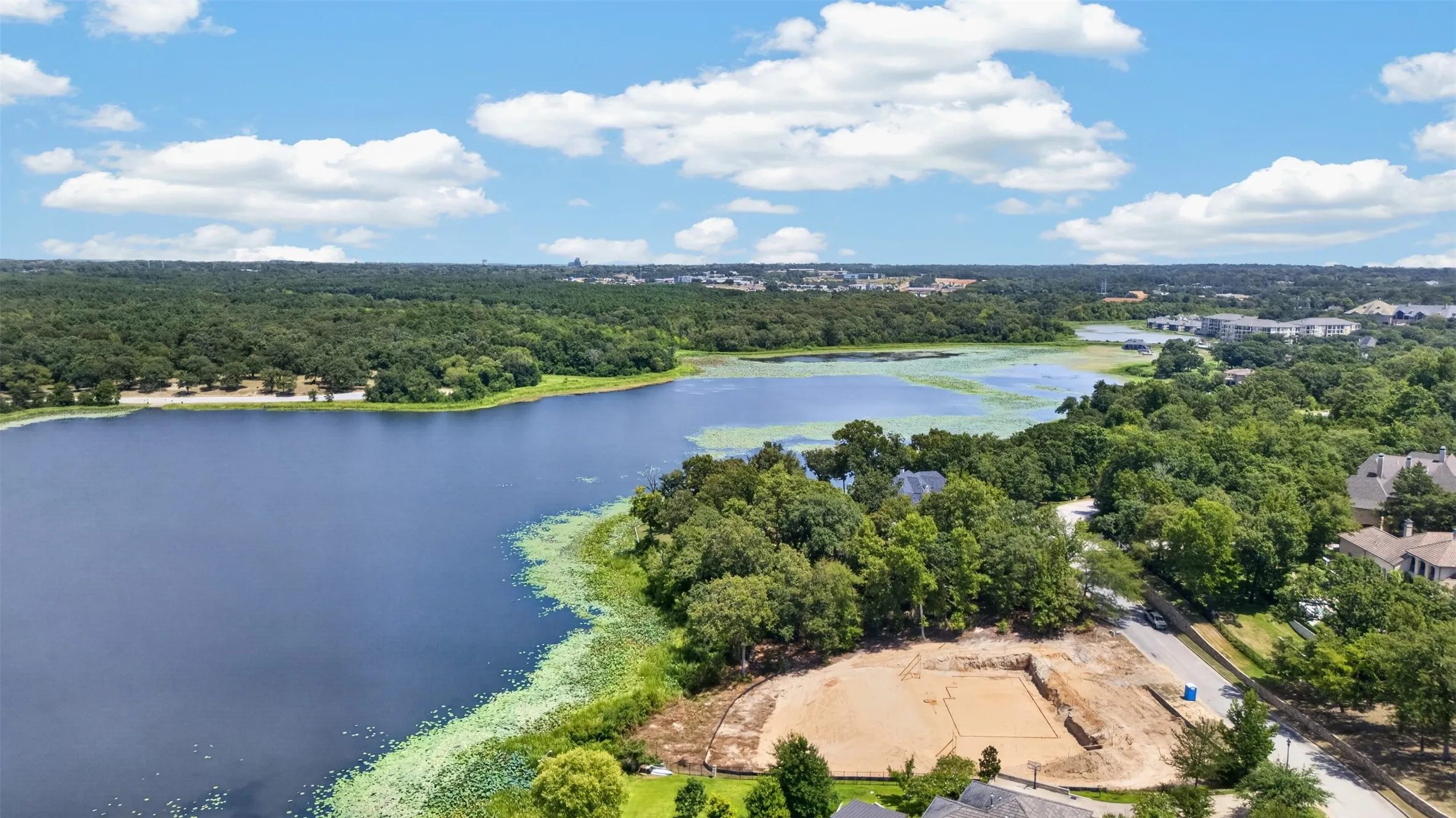 Expansive waterfront property featuring mature trees, a paved road, and a substantial body of water