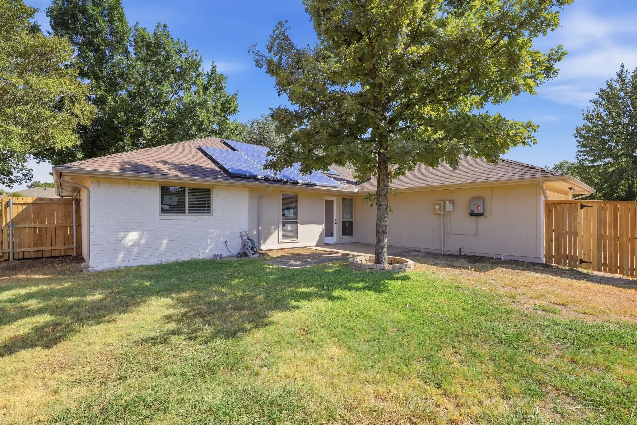 Single-story residence featuring a clean white exterior with a metal roof, set on a spacious lot with mature shade trees