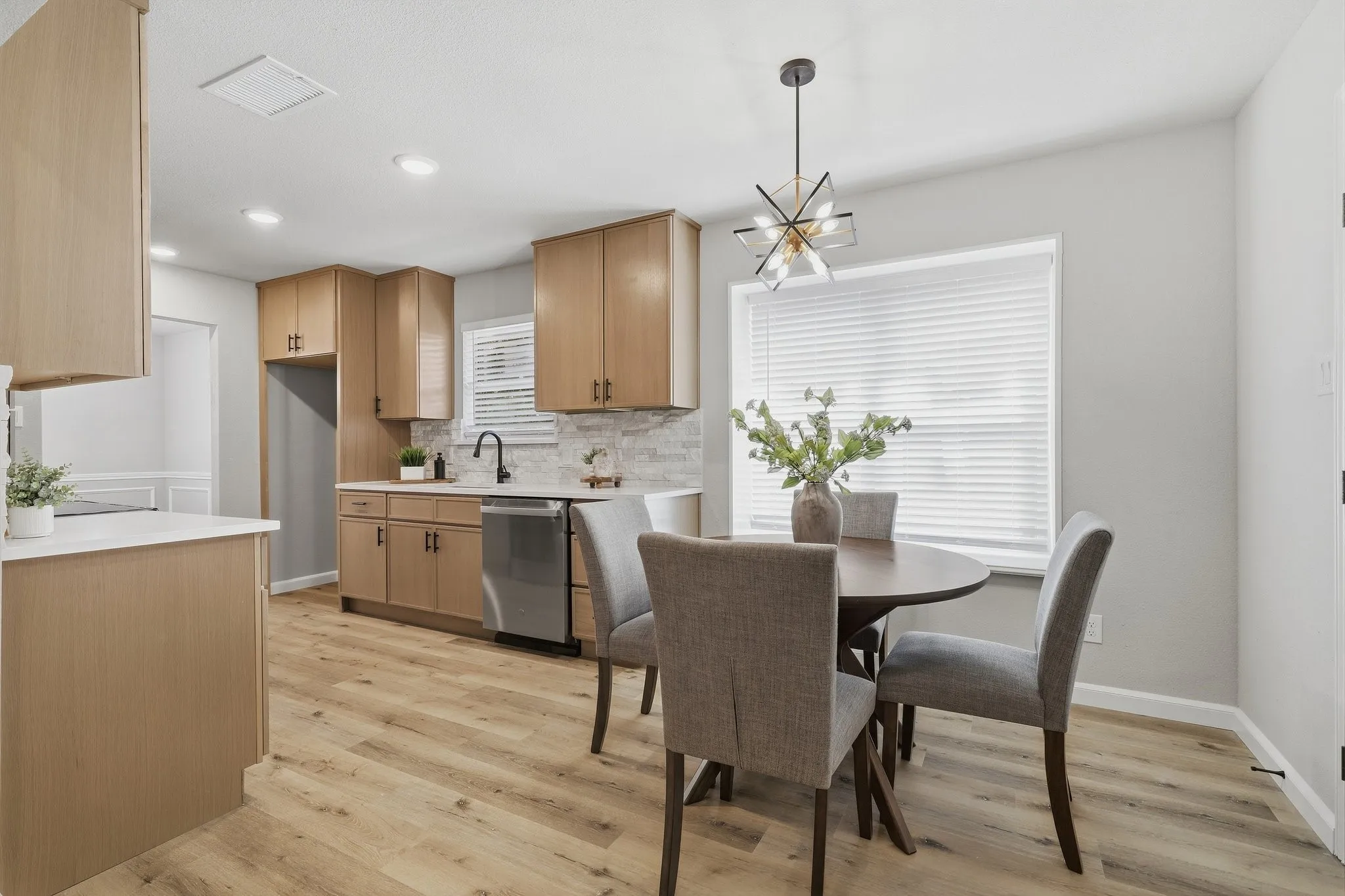 Wood-finish flooring throughout, light wood cabinetry, stone-finish backsplash, stainless steel appliances, and a contemporary ceiling fixture