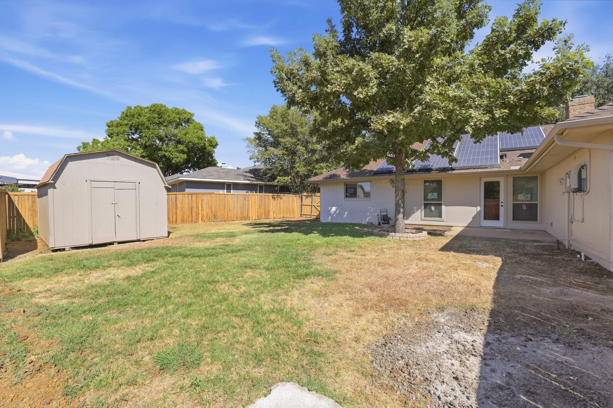 Expansive backyard with a wooden fence, storage shed, and a concrete patio