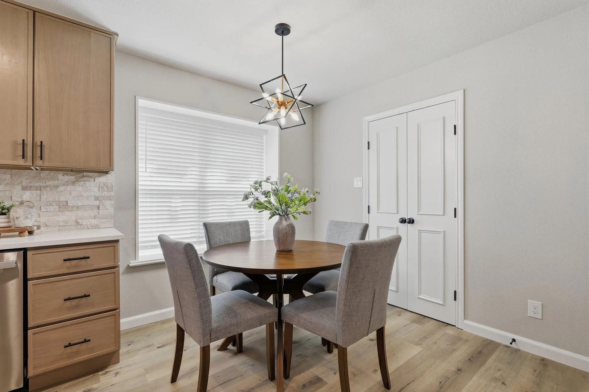 Wood-finish flooring, light wood-tone cabinetry, white countertop, stone tile backsplash, and a contemporary light fixture