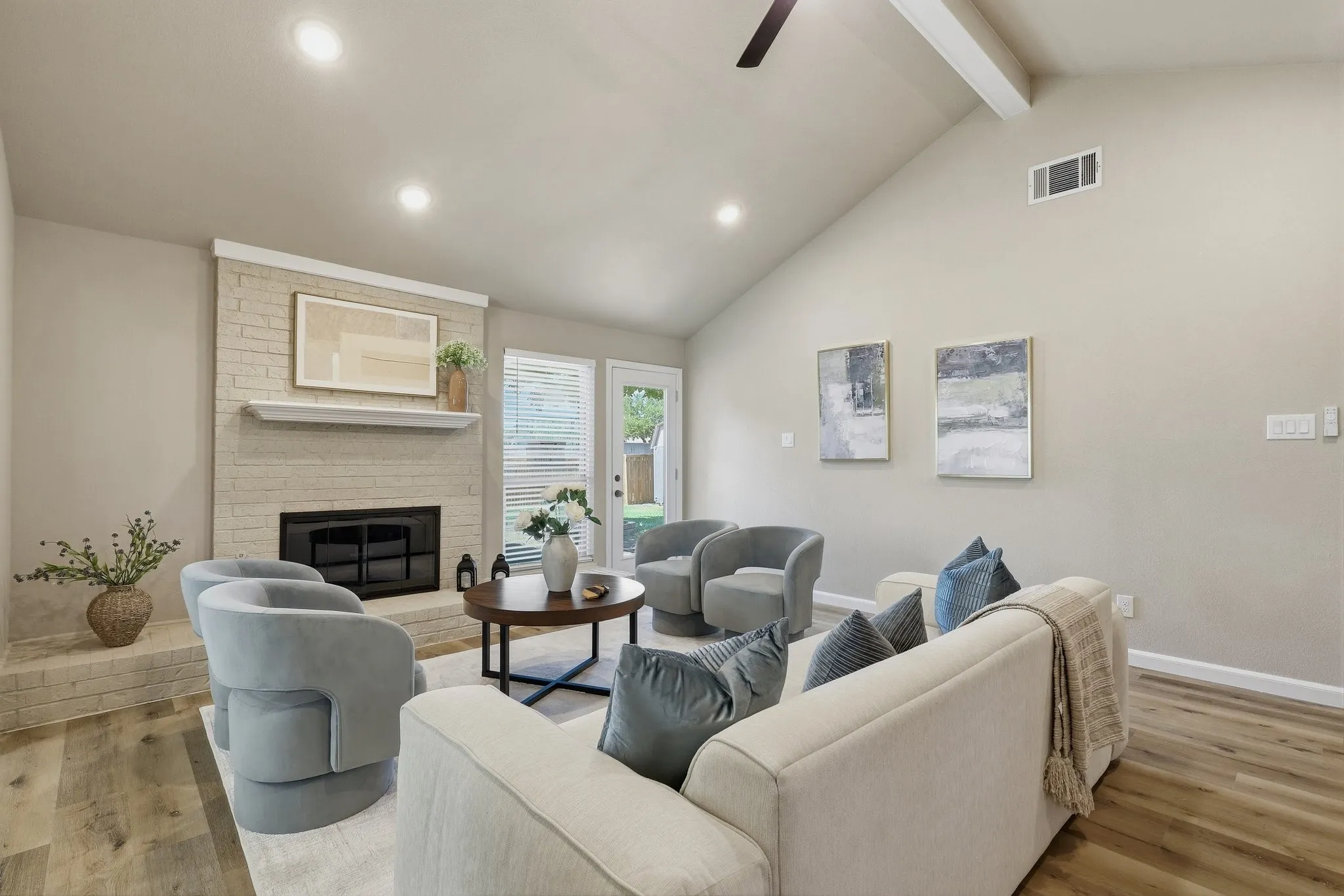 Vaulted ceiling with exposed beam, recessed lighting, brick-clad fireplace with mantel, wood-finish flooring, and exterior access via glass-paneled door